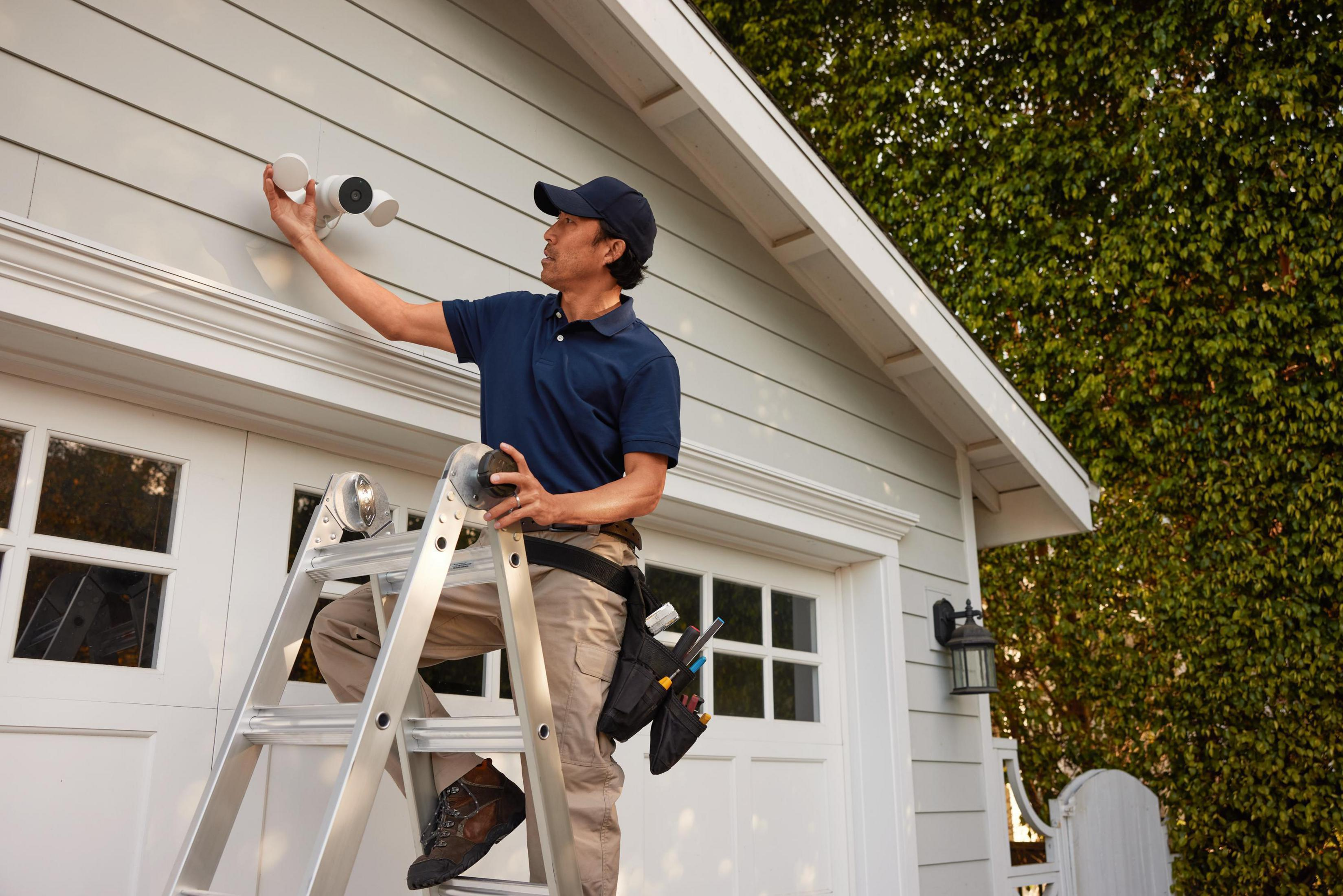 Mężczyzna na drabinie instaluje kamerę bezpieczeństwa na domu.