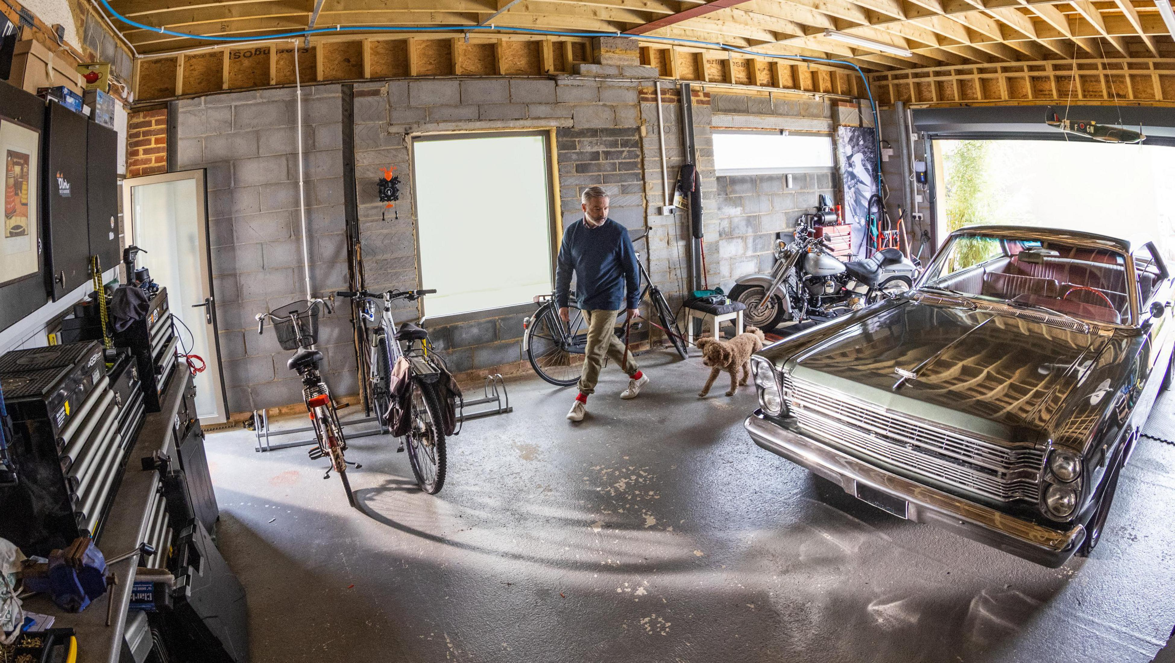 Wnętrze garażu z mężczyzną, psem, samochodem i rowerami. Drzwi garażowe są otwarte.