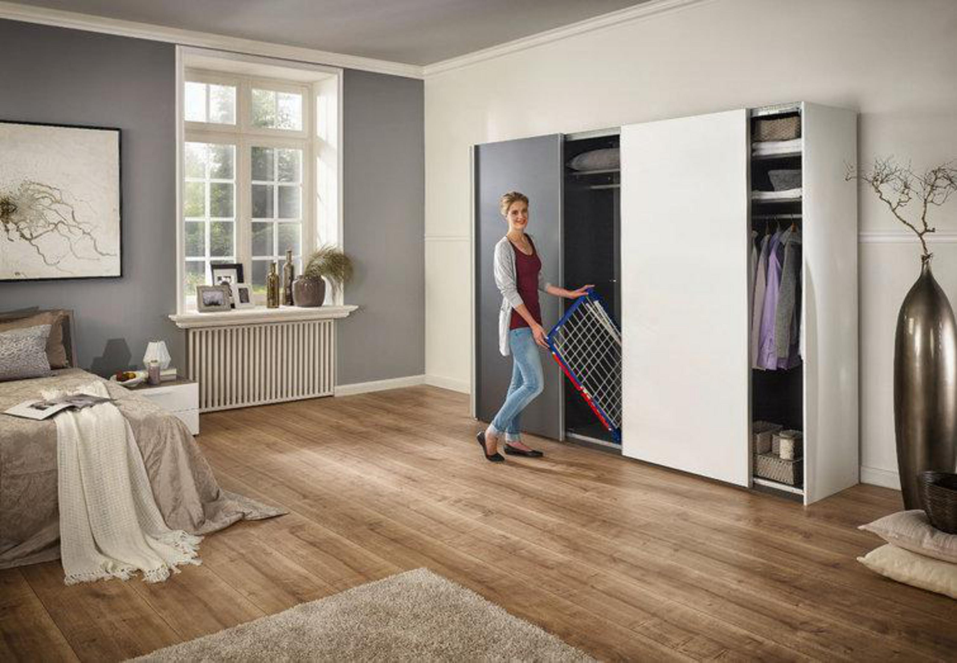 Eine Frau in einem Schlafzimmer öffnet einen Schrank mit einem Wäschegestell.