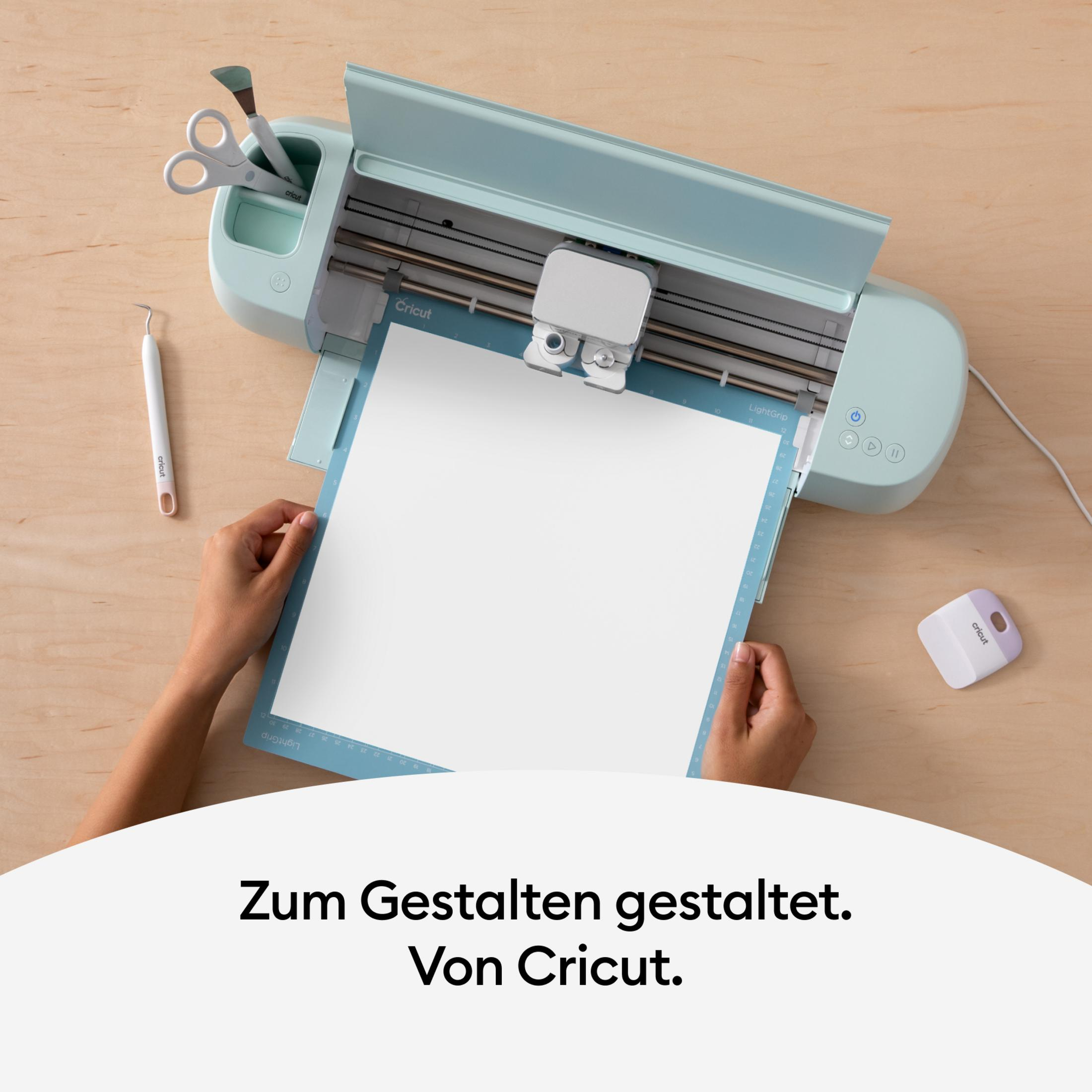 Hände benutzen Cricut-Maschine mit Papier, Klingen und Werkzeugen auf Holz.
