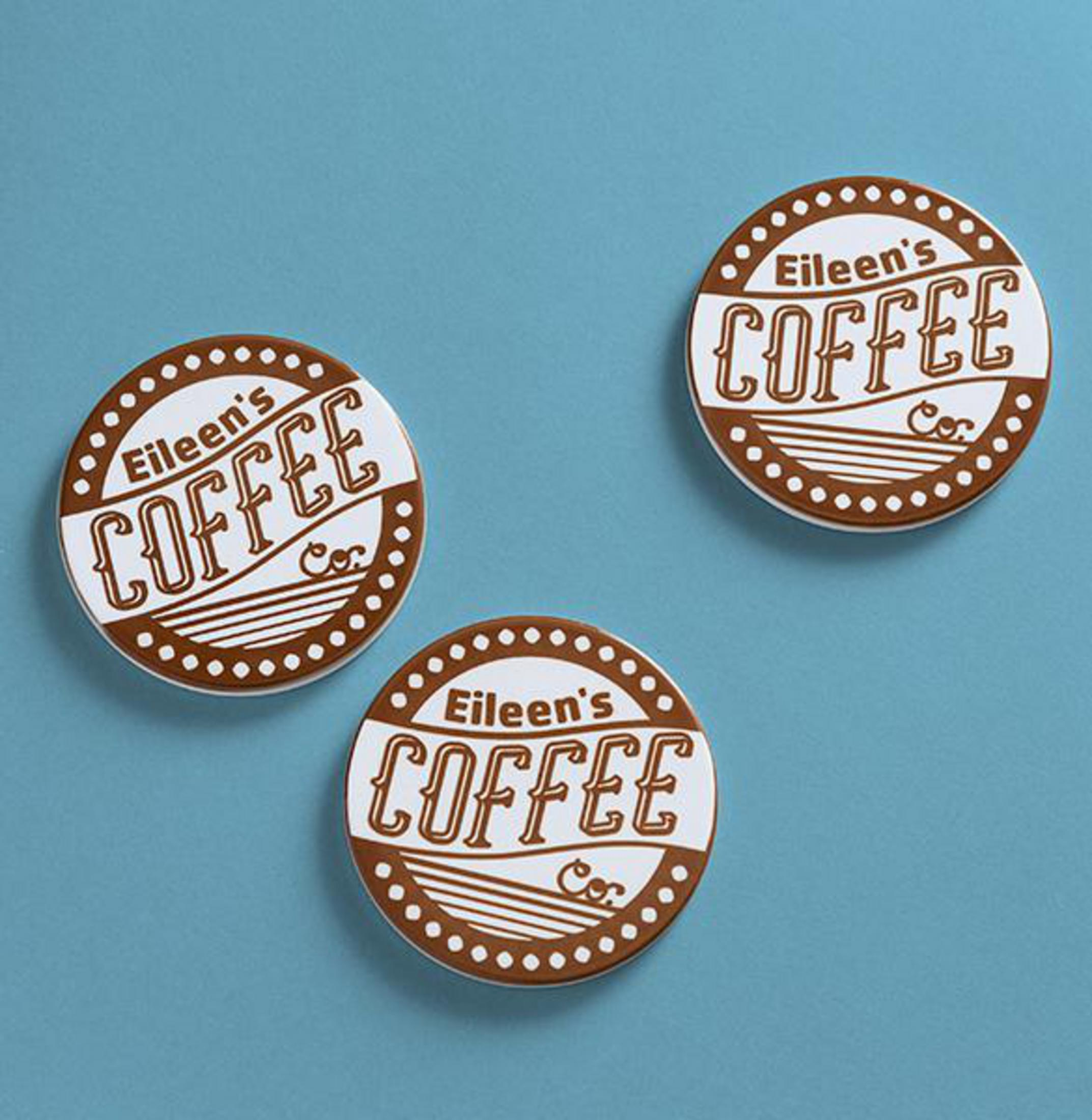 Drei Eileen's Coffee-Untersetzer auf blauem Untergrund. Braun-weißes Design mit Kaffeetasse.