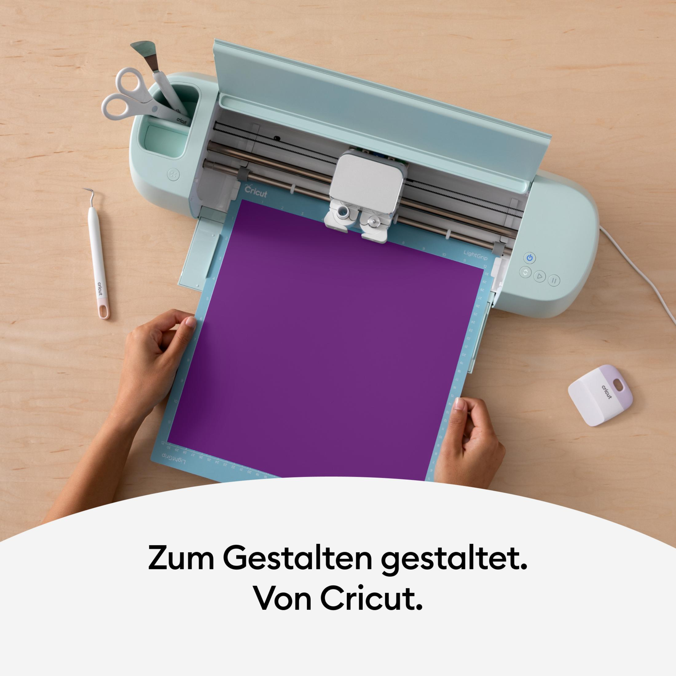 Eine Cricut-Maschine mit einer lila Schneidematte. Hände legen ein lila Papier darauf.