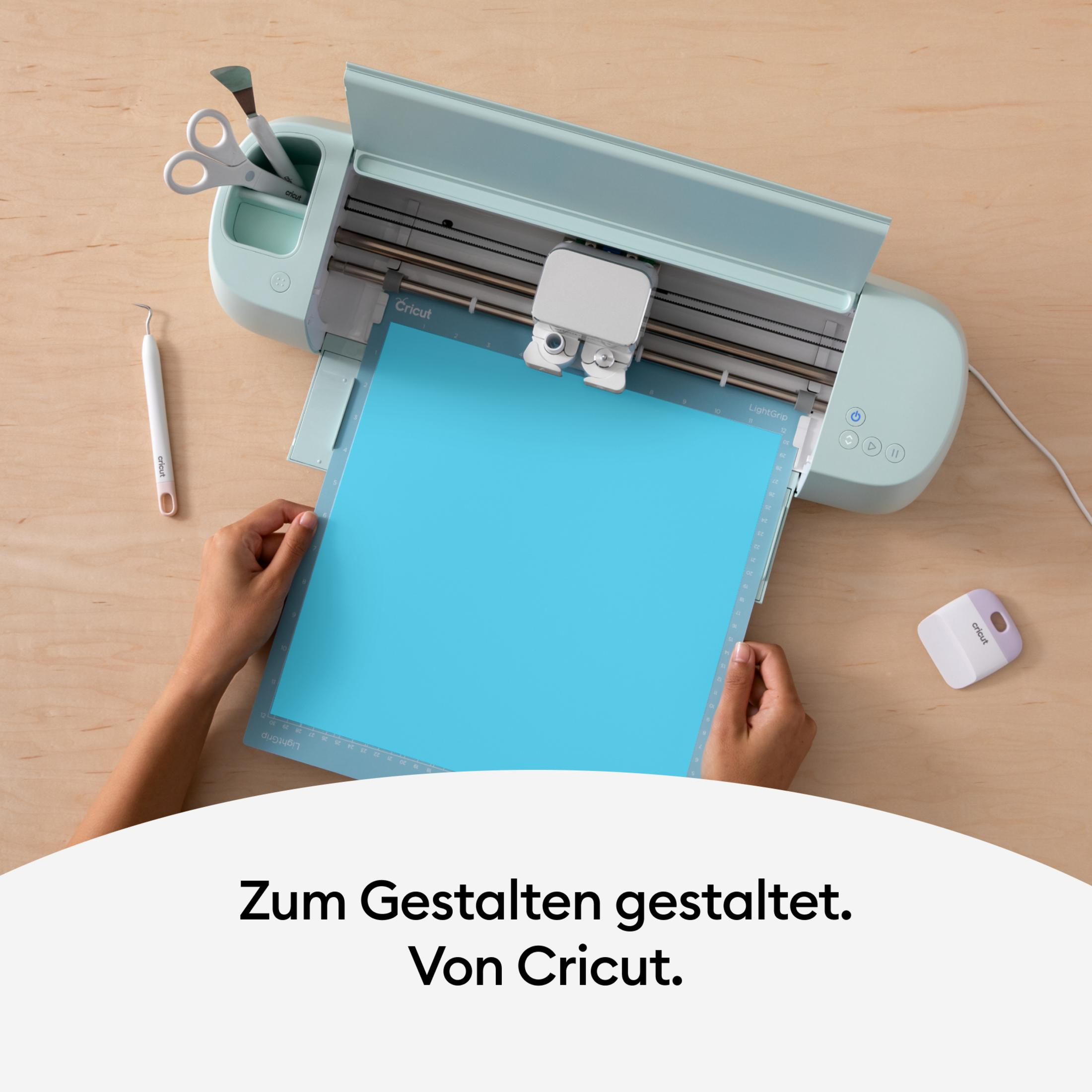 Hände bedienen Cricut Maschine, blaue Schneidematte und Text darunter.