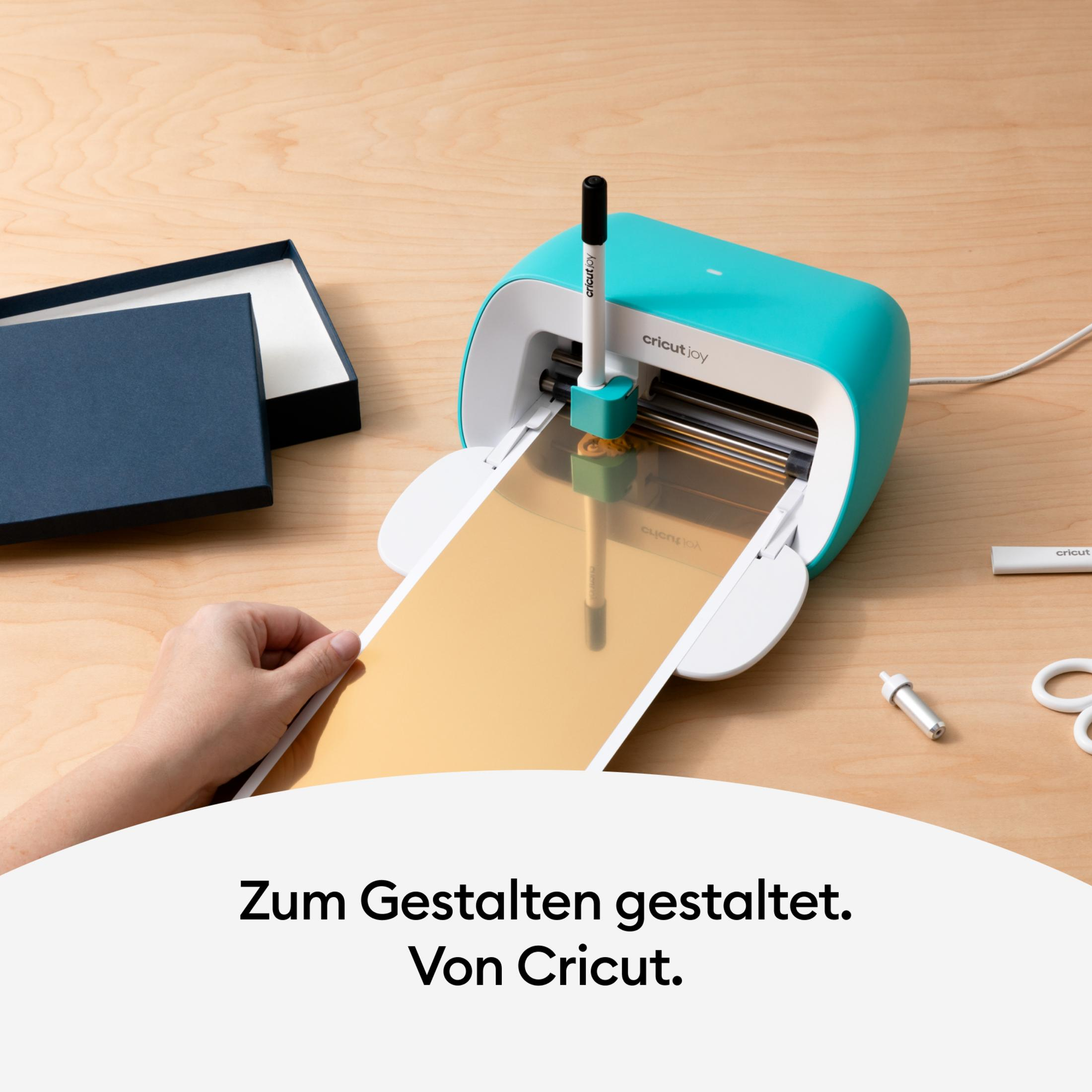 Eine Cricut Joy Maschine, in die ein goldenes Blatt eingelegt wird. Eine Hand führt das Blatt ein.
