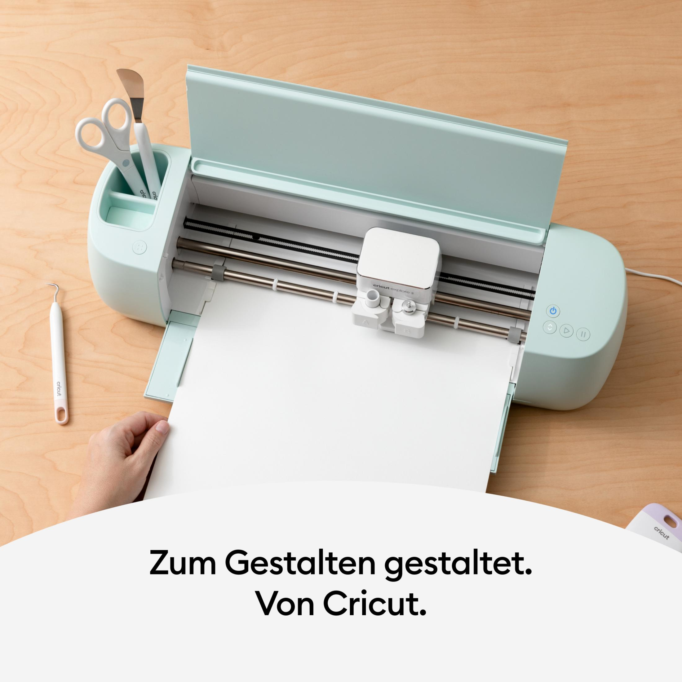 Eine Cricut-Maschine mit weißem Papier. Schere und andere Werkzeuge befinden sich auf der rechten Seite.