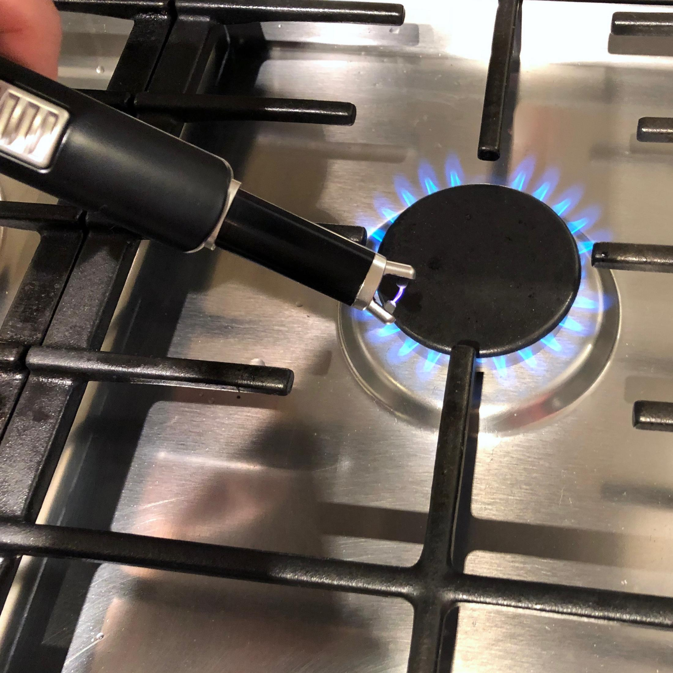 Eine Hand, die ein Feuerzeug hält und einen Gasbrenner mit blauen Flammen entzündet.