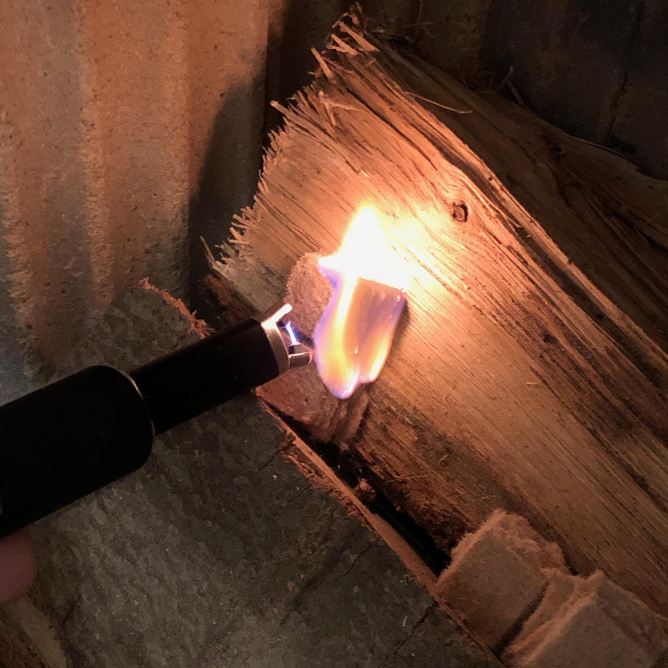 Ein Feuerzeug entzündet einen Holzblock. Orange Flamme, dunkler Hintergrund.