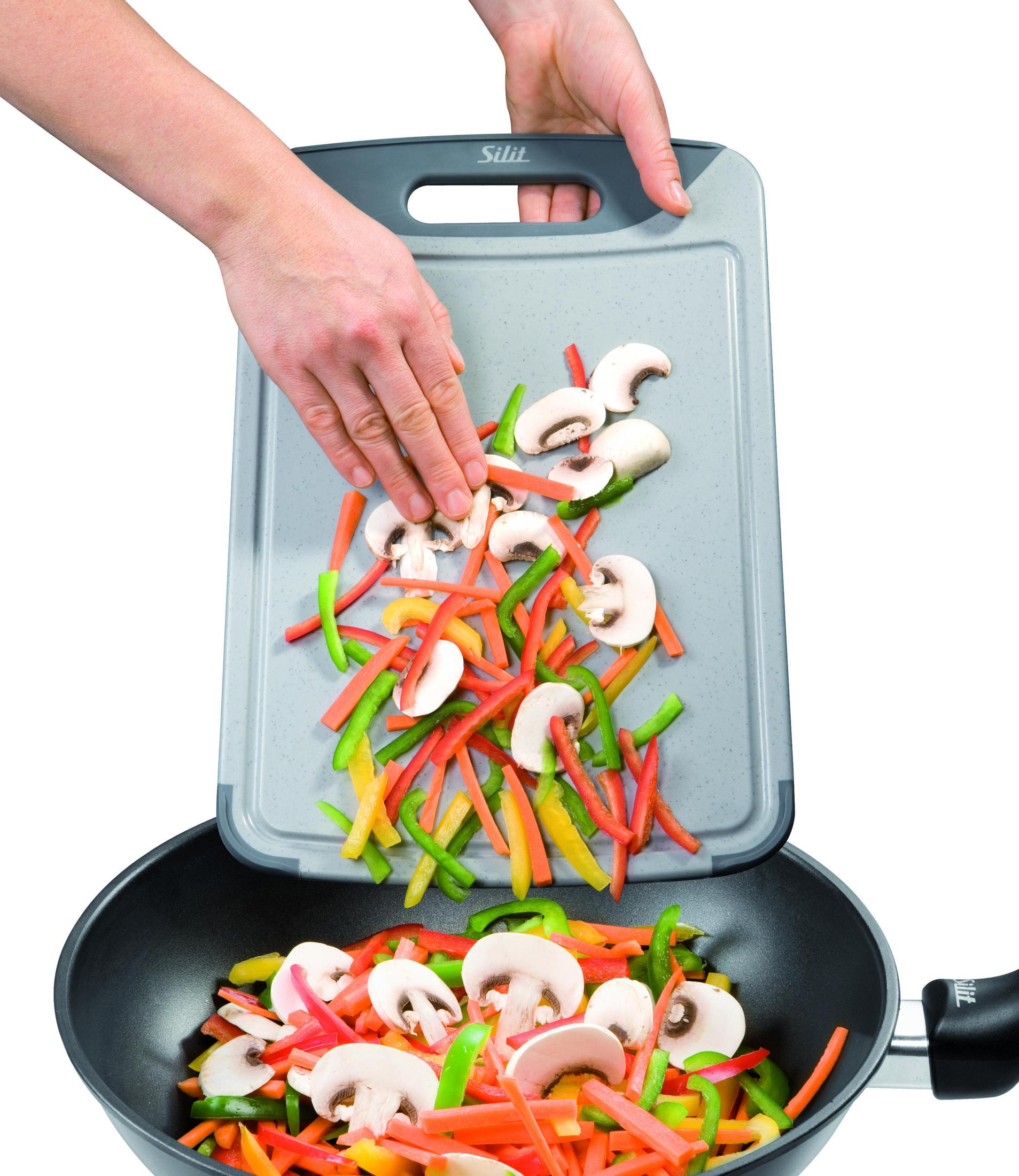 Hände gießen geschnittenes Gemüse vom Schneidebrett in den Wok.