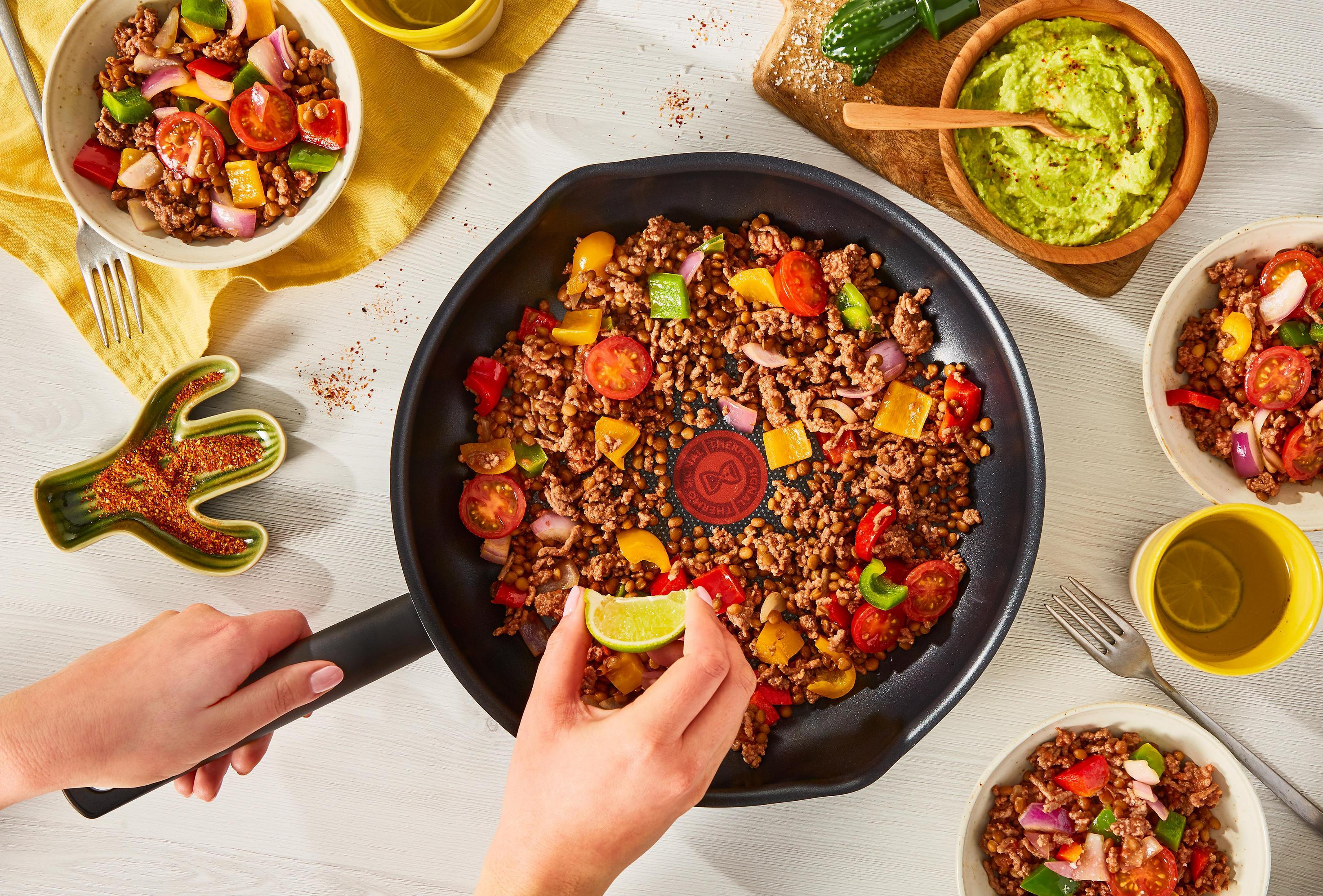 Widok z góry na patelnię z gotowanym jedzeniem, pomidorami, papryką i limonką. Miski wokół.