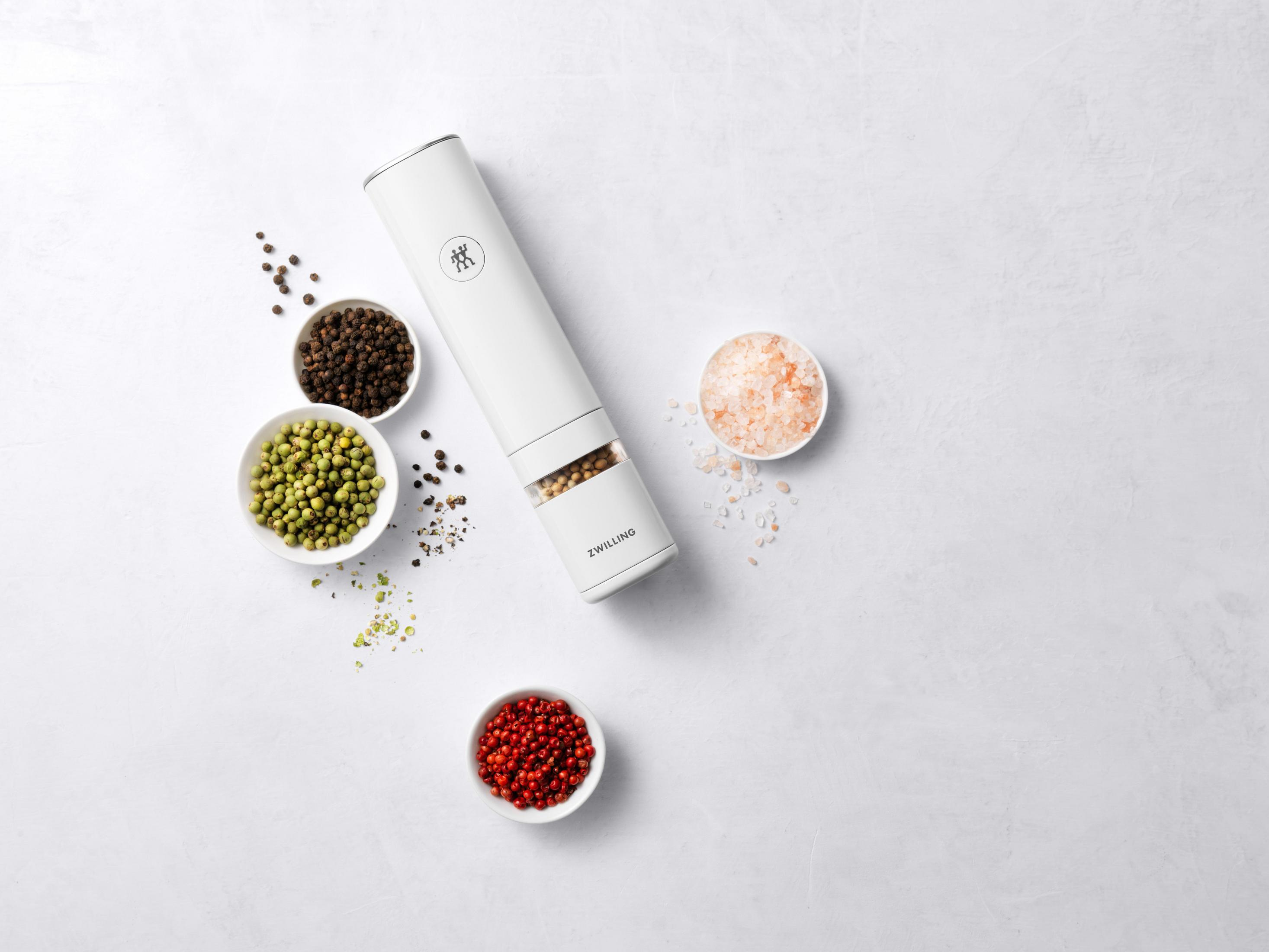 Biały młynek do pieprzu z miseczkami pieprzu i soli. Białe tło.