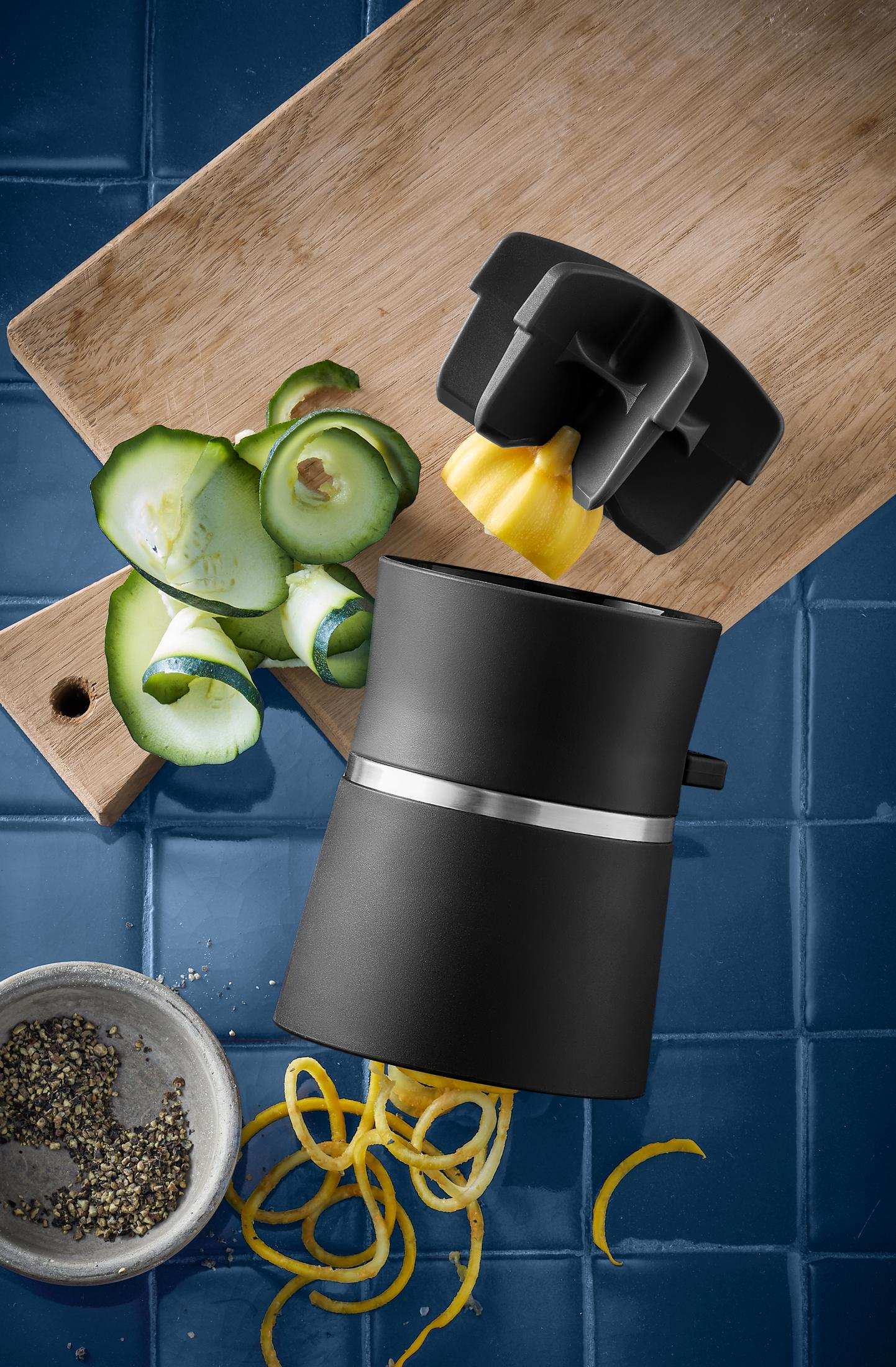Ein schwarzer Spiralschneider mit Zucchinispiralen auf blauer Fliese.