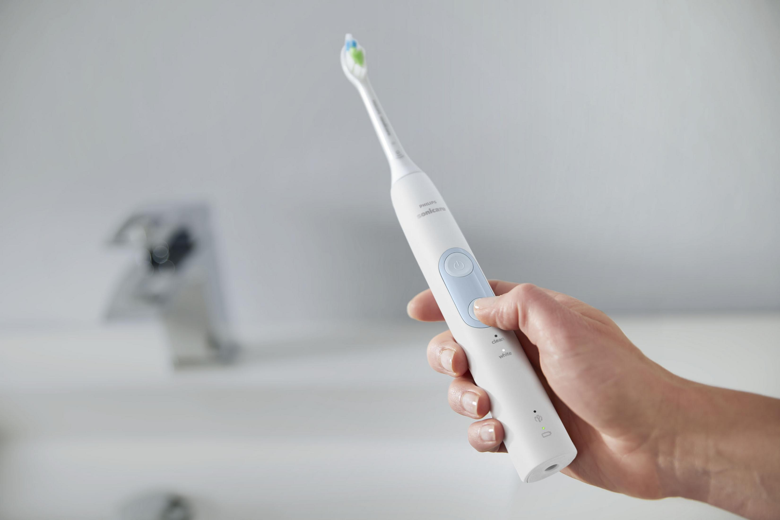 Eine weiße elektrische Zahnbürste in der Hand einer Person, Badezimmerhintergrund.