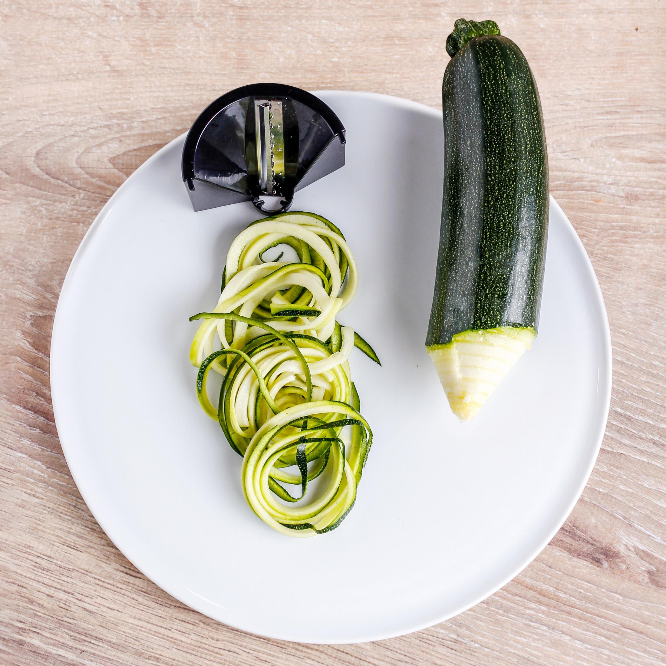 Courgette noodles op een wit bord met een courgette en een spiraalsnijder.
