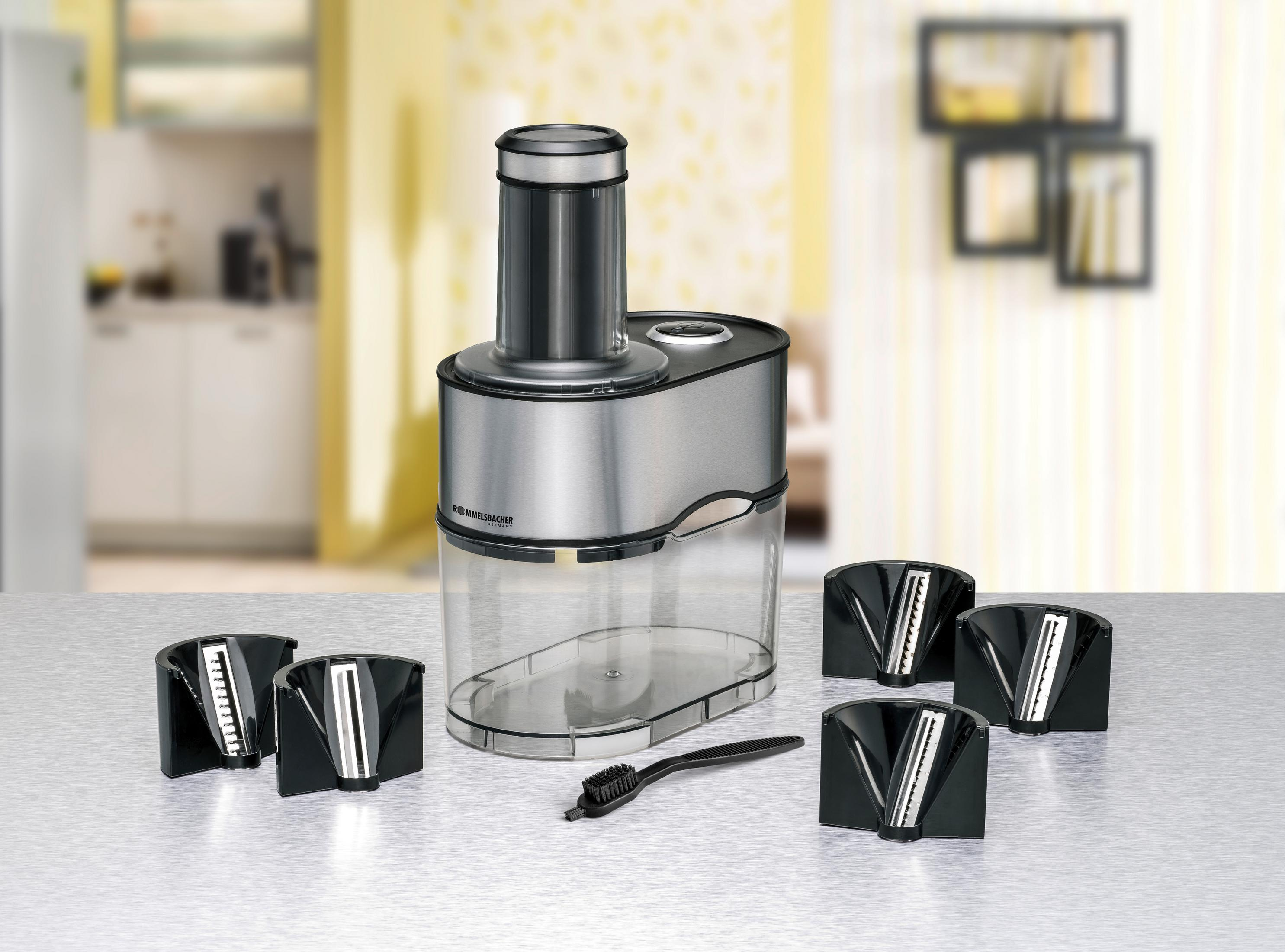 Een keukenmachine met messen en accessoires op een aanrecht. De behuizing is zilver en doorzichtig.
