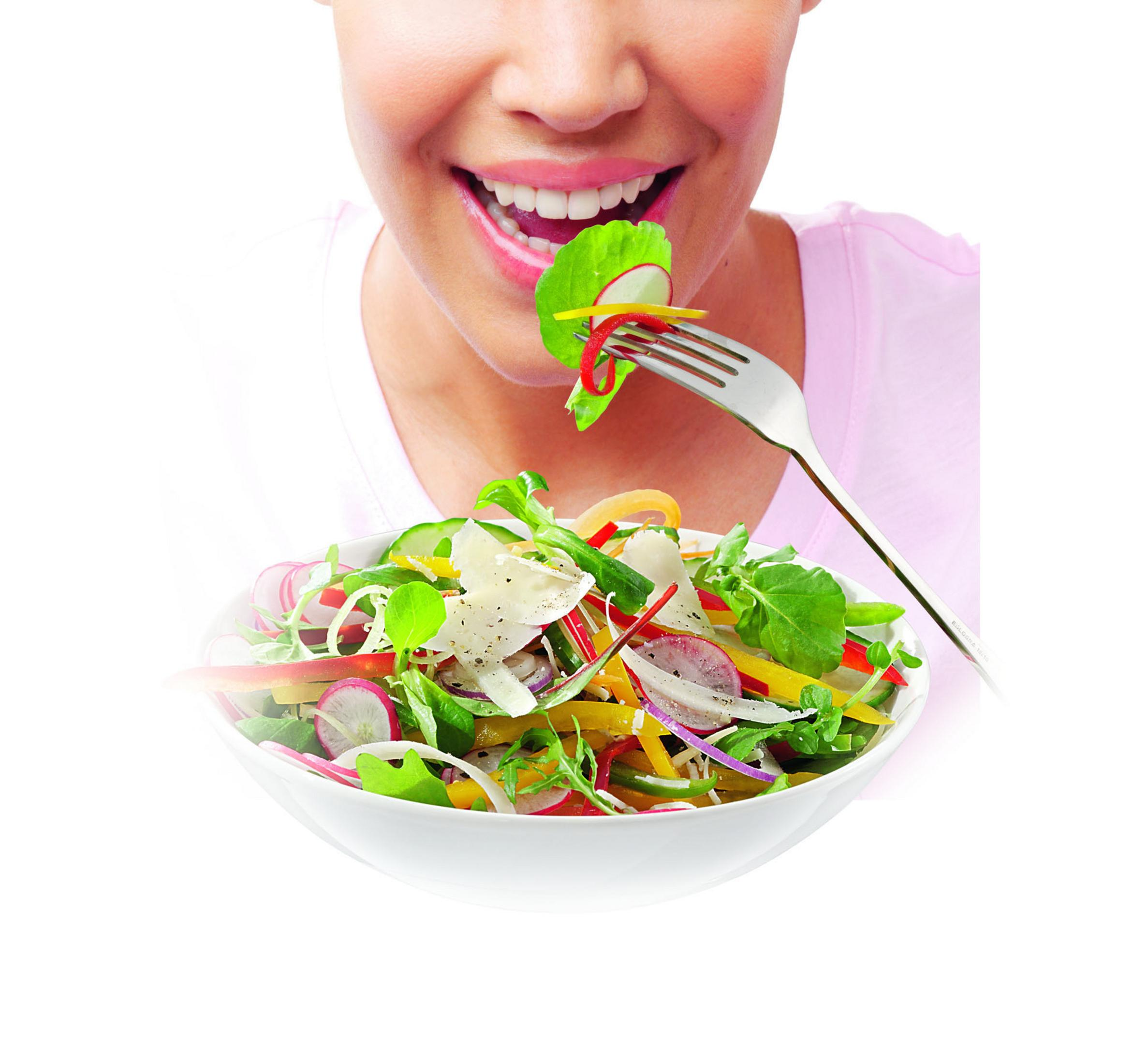 Person eating salad with a fork, smiling.