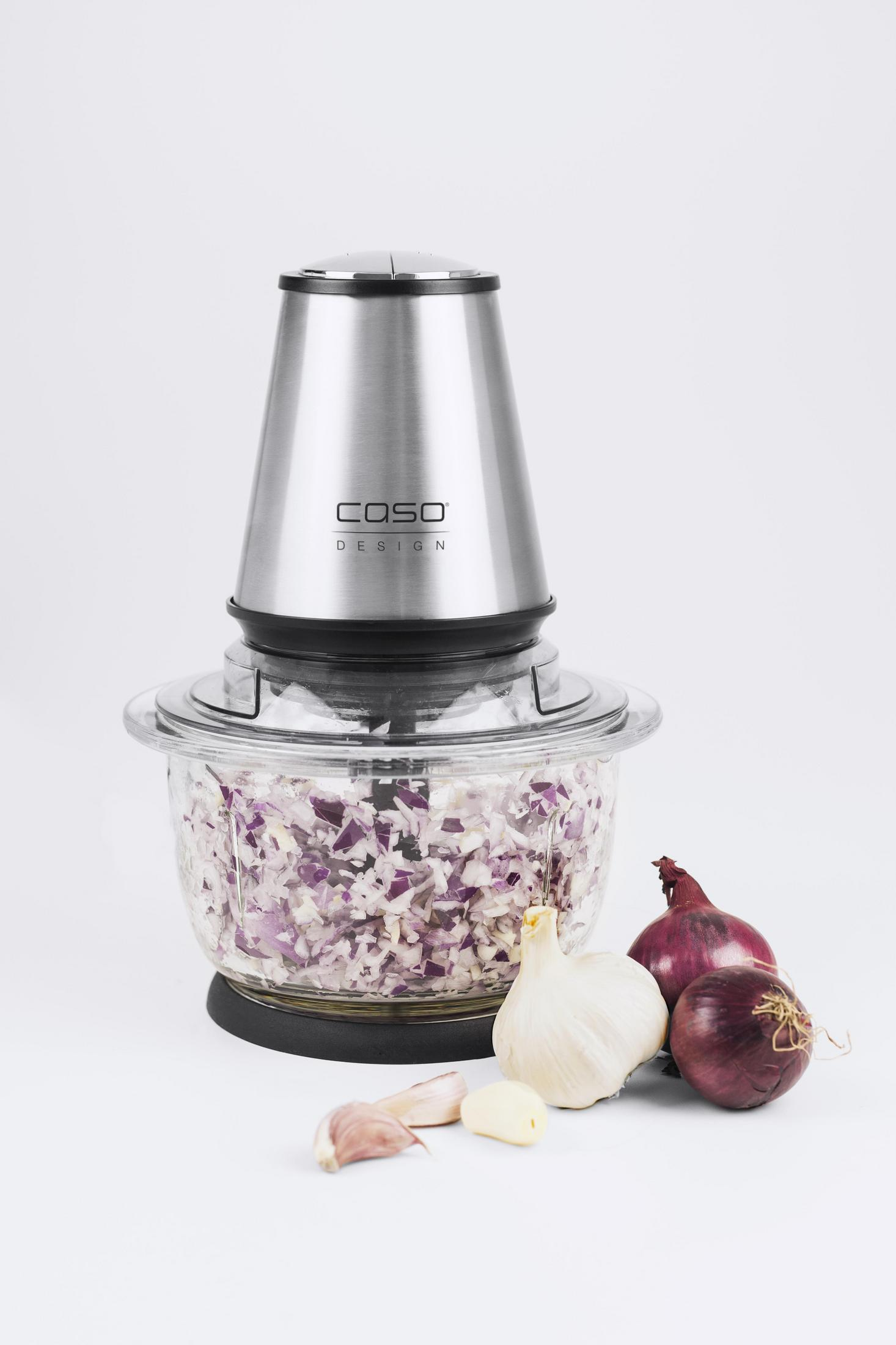 Robot da cucina, acciaio inox, cipolle rosse tritate, aglio e cipolle intere su sfondo bianco.