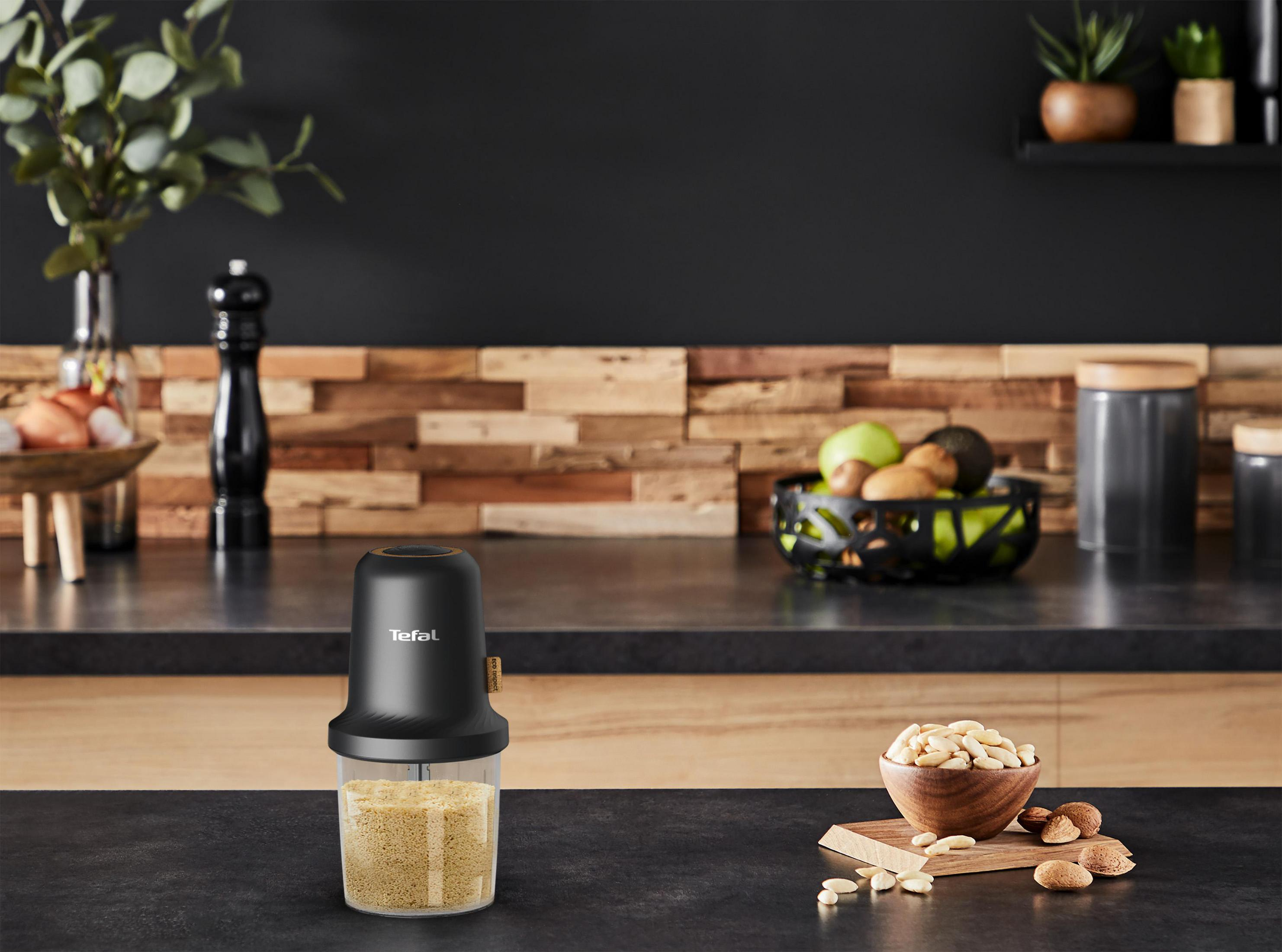 Scena cucina con robot da cucina nero, noci in una ciotola e alzatina in legno.