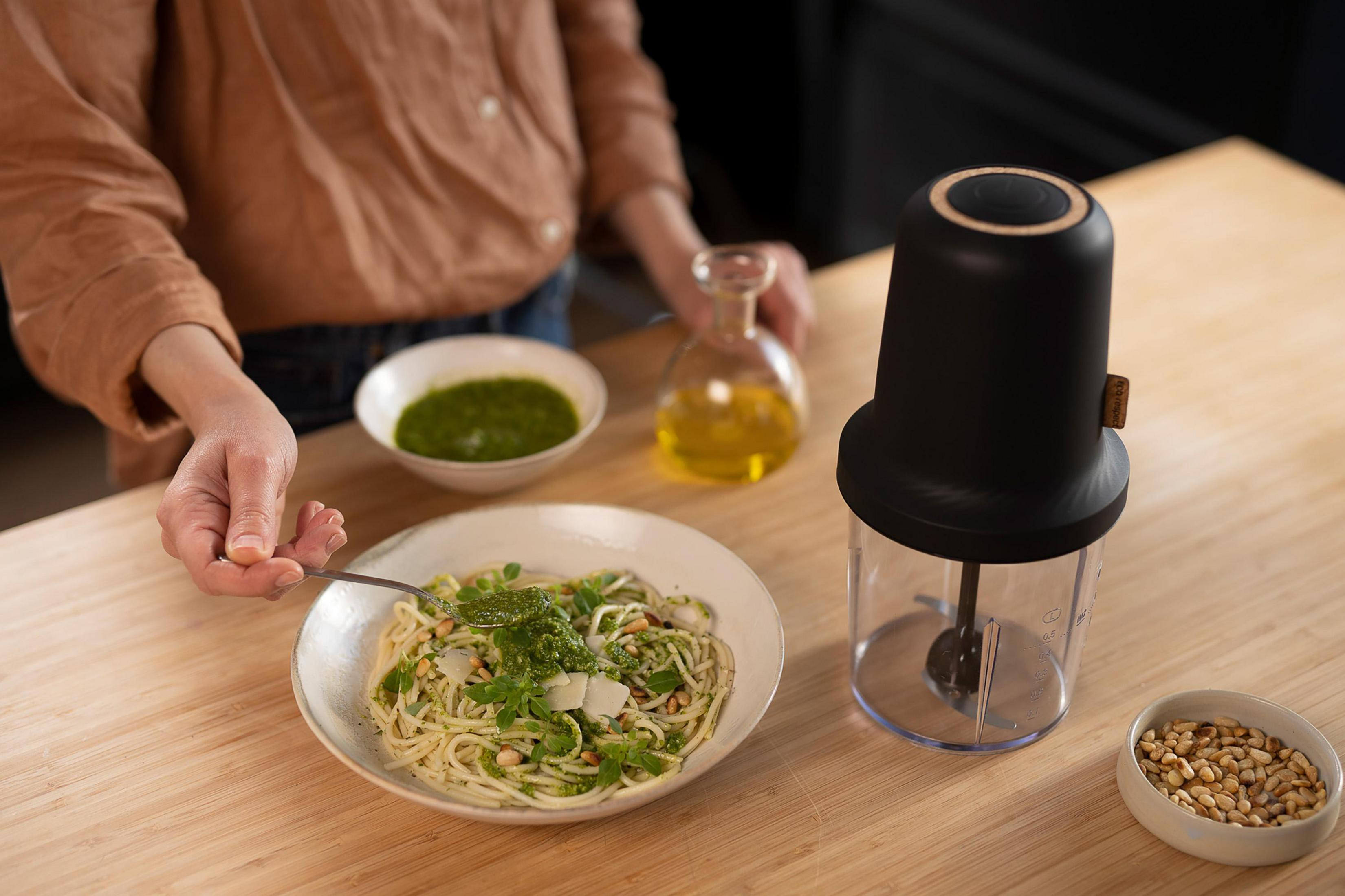 Una persona aggiunge pesto agli spaghetti. Ingredienti: pesto, pasta, olio d'oliva e pinoli.