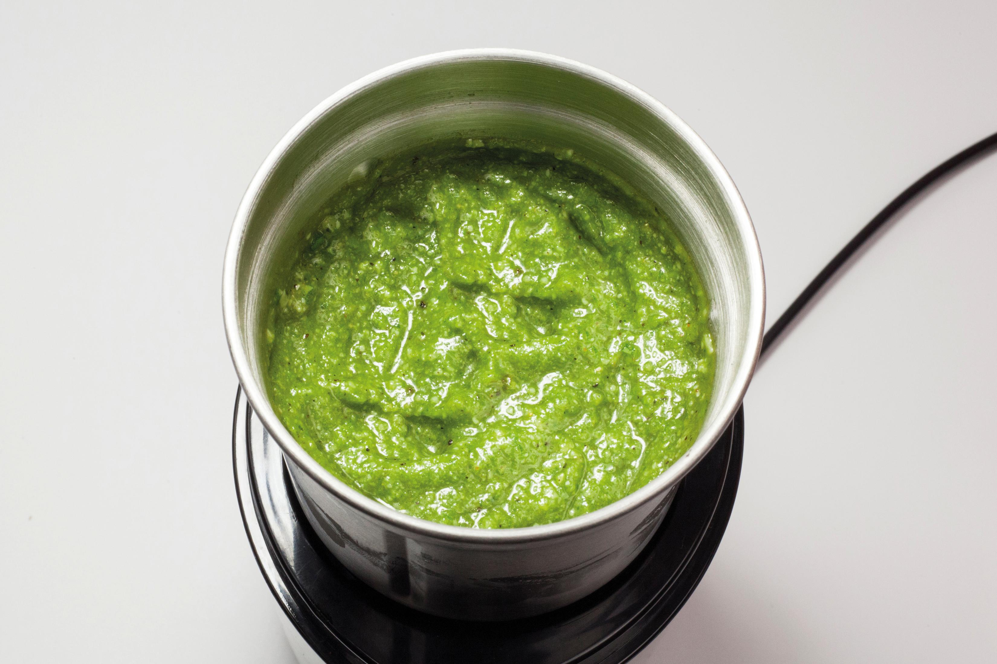 Primo piano di pesto verde in una ciotola d'argento. La ciotola è su una base nera, su una superficie bianca.