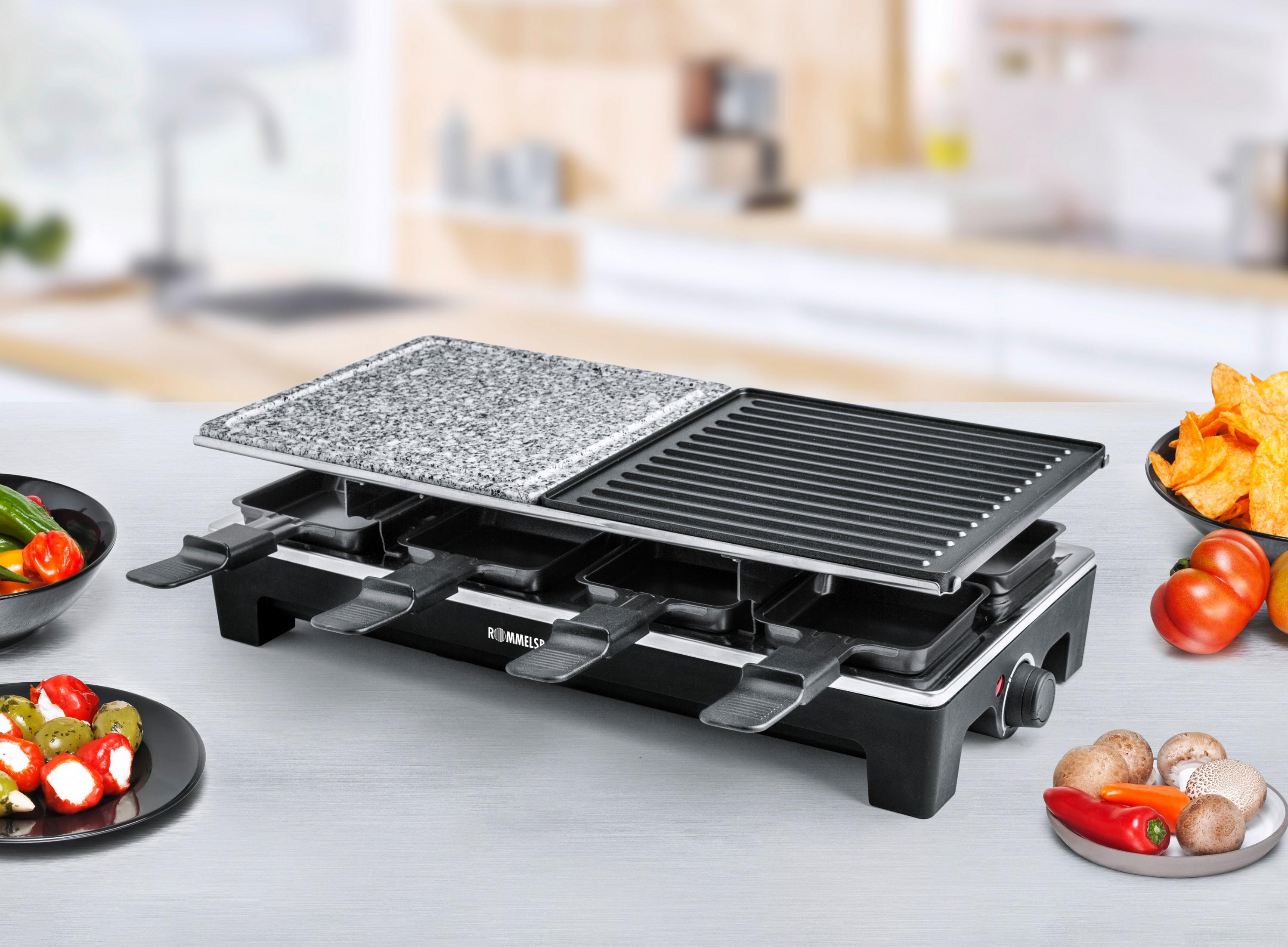 Grill do raclette z jedzeniem, talerzami warzyw i rozmytym tłem kuchni.