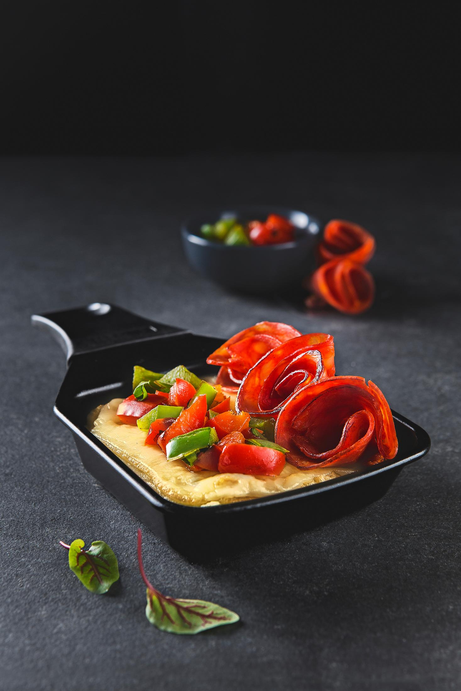 Naczynie z jedzeniem: ser, róże z czerwonej papryki, zielona papryka i pomidory. Ciemne tło.