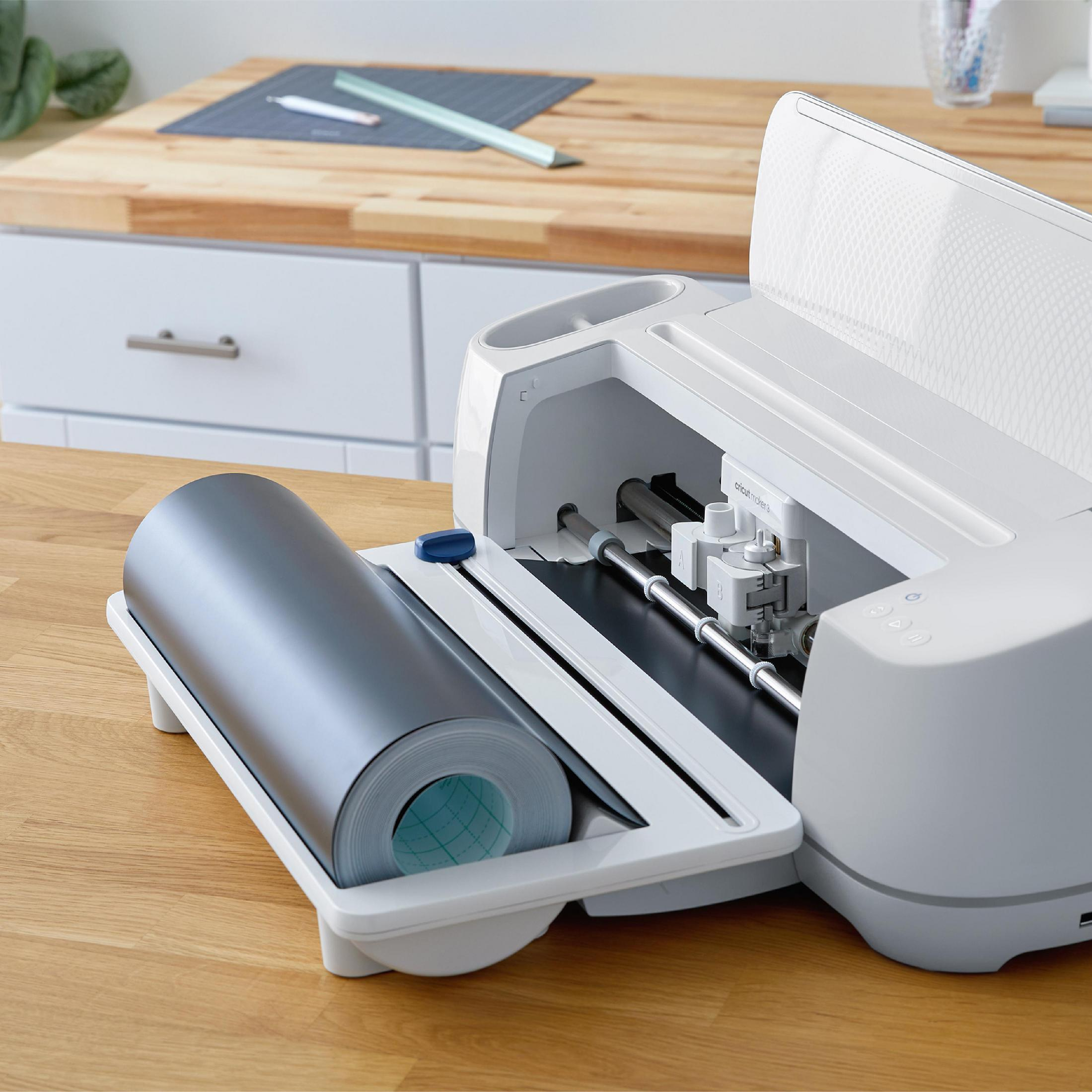 Weiße und graue Bastelmaschine mit einer Rolle grauen Materials auf einer Holzoberfläche.