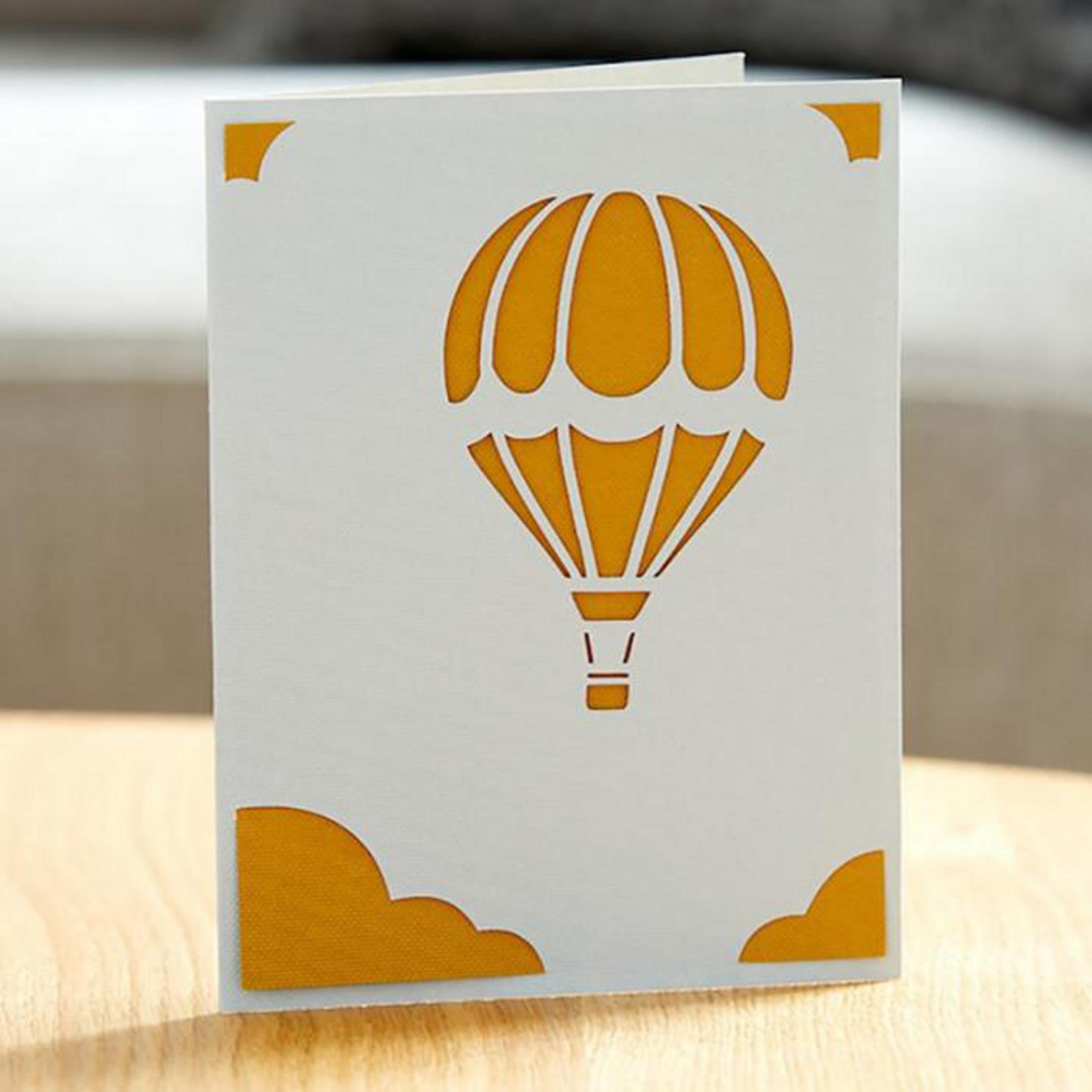 Grußkarte mit einem ausgeschnittenen Heißluftballon-Design, gelb auf weiß.
