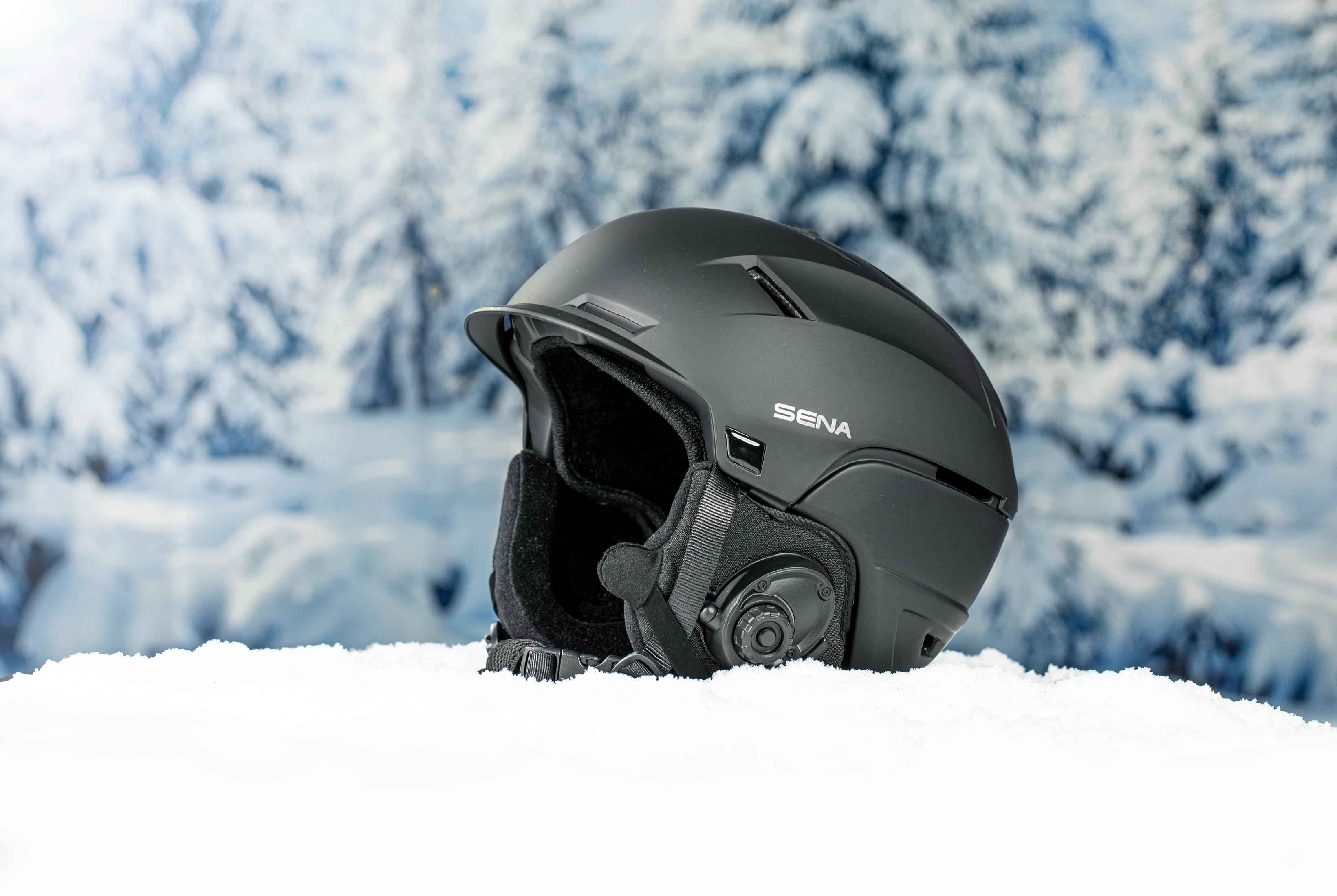 Un casco de esquí negro sobre la nieve. El fondo muestra un bosque nevado.