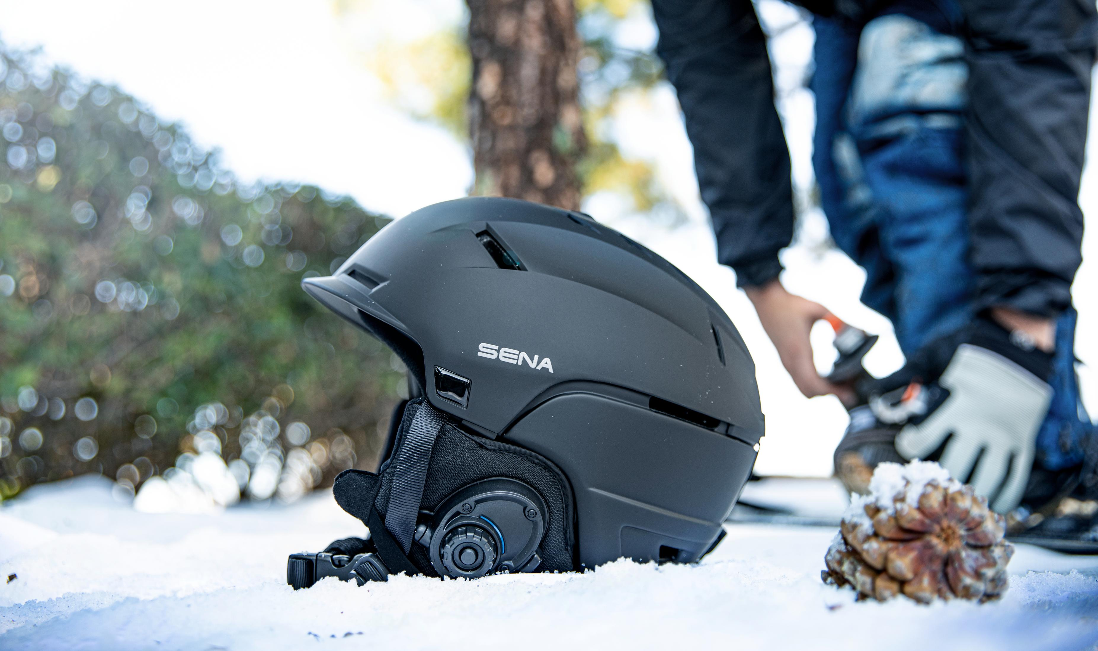 Un casco de esquí Sena negro sobre la nieve. Una persona en jeans y chaqueta se prepara para ponérselo.