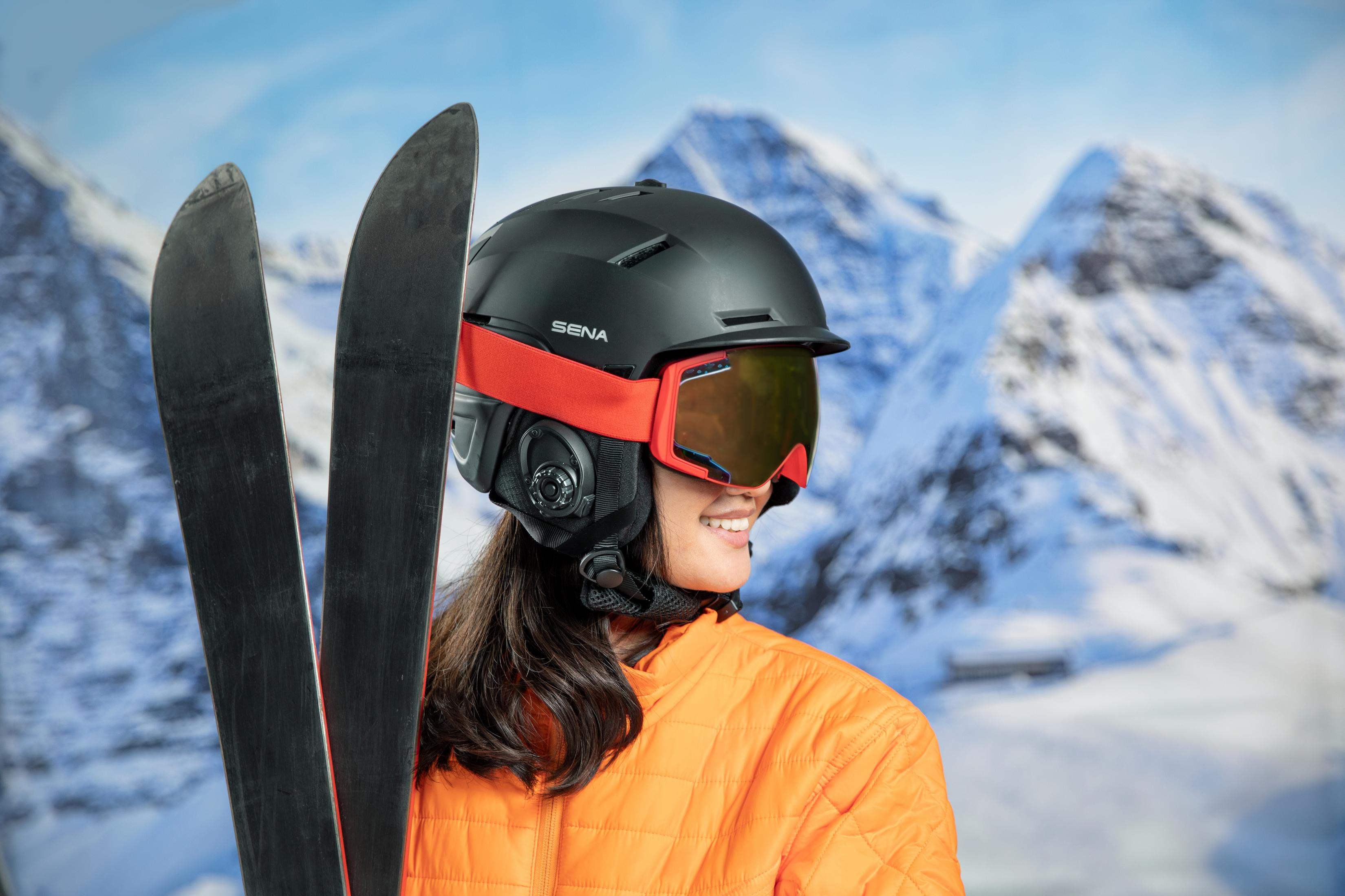 Una persona con un casco de esquí negro con detalles rojos y visera. Esquís y montañas nevadas al fondo.