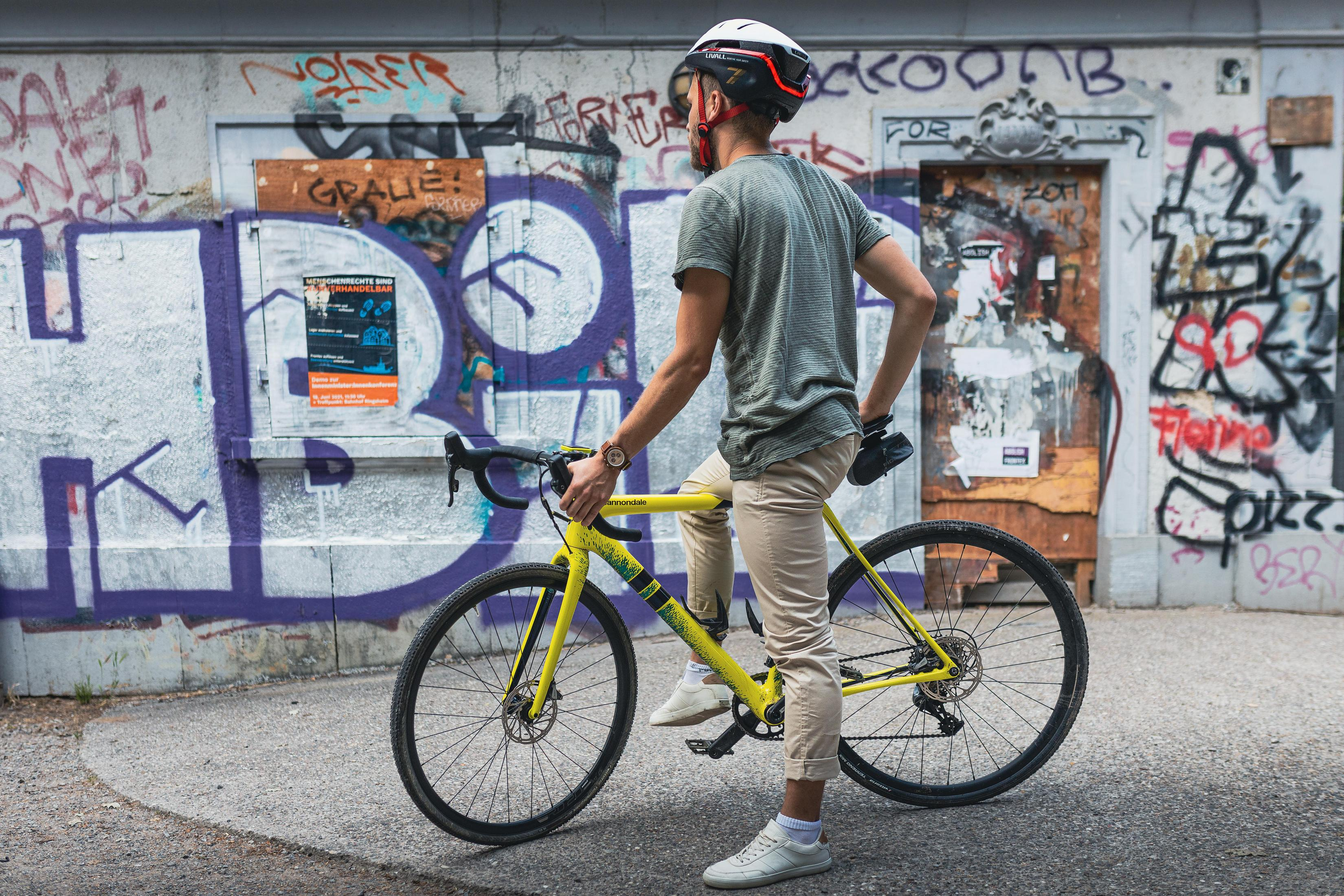 Uomo in casco accanto a bici gialla contro un muro con graffiti.
