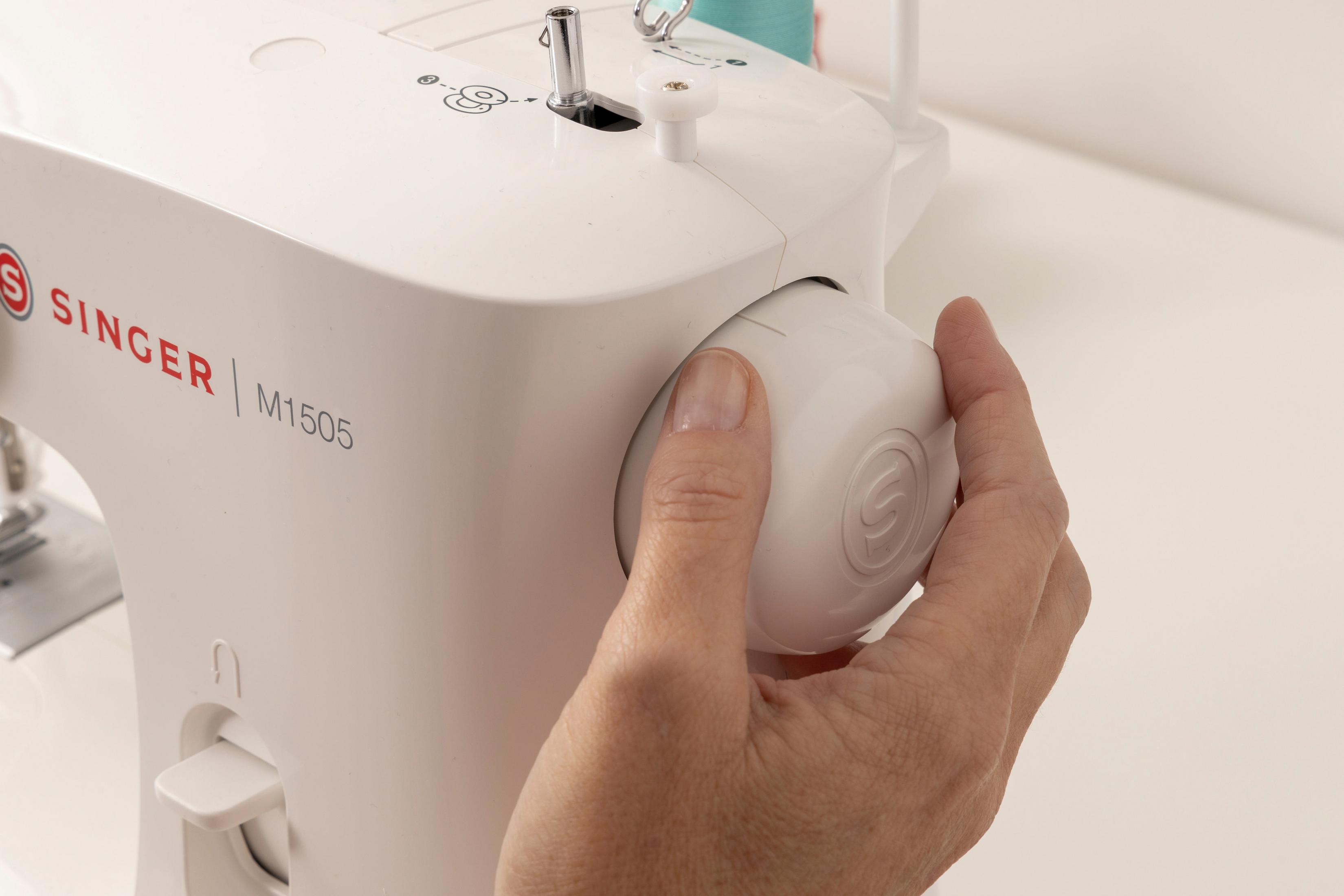 Zbliżenie dłoni obracającej białe pokrętło na białej maszynie do szycia Singer, model M1505.