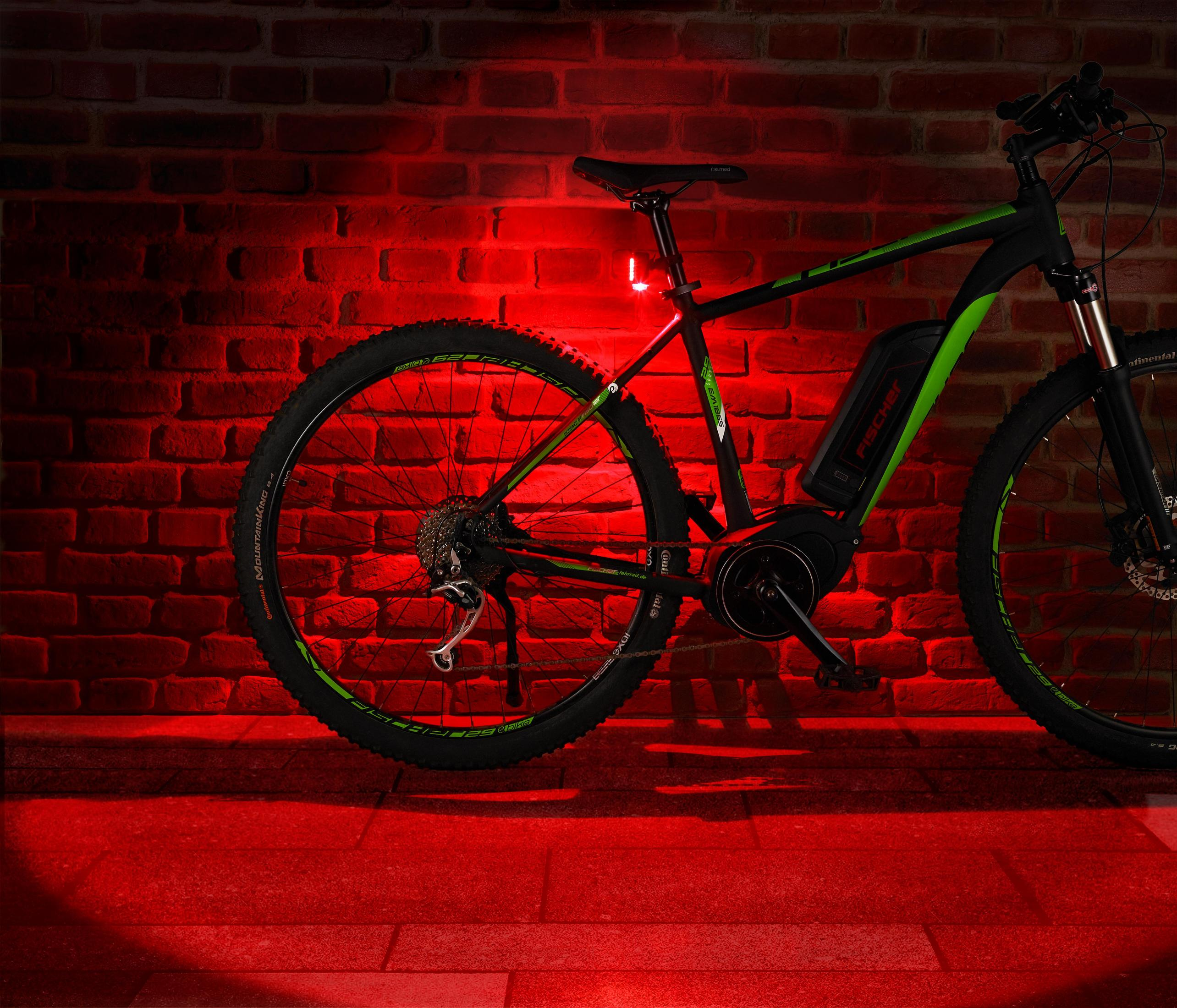 Ein schwarz-grünes Elektrofahrrad mit rotem Licht vor einer Backsteinmauer.