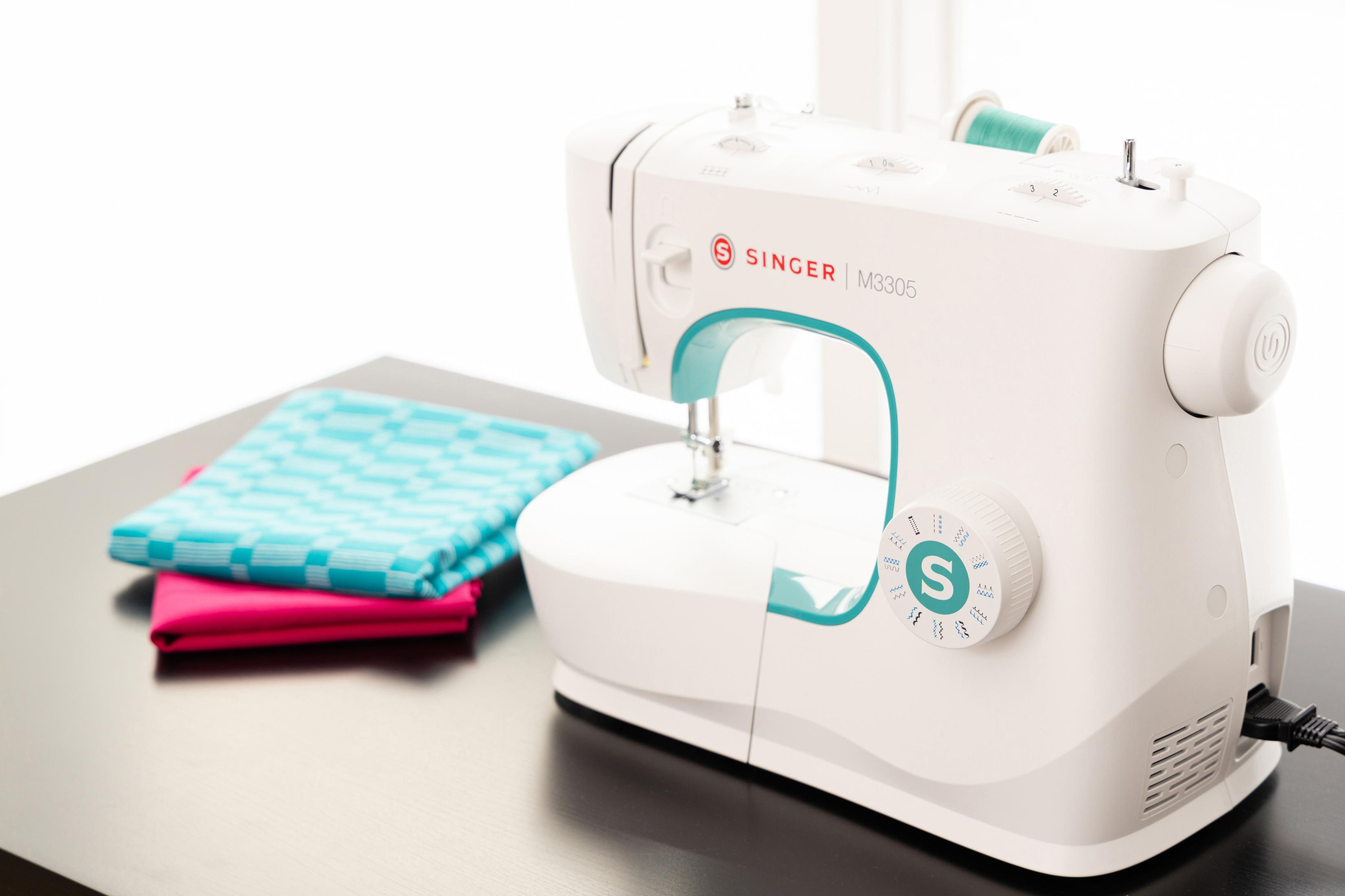Biała maszyna do szycia z turkusowymi akcentami, materiał po lewej.