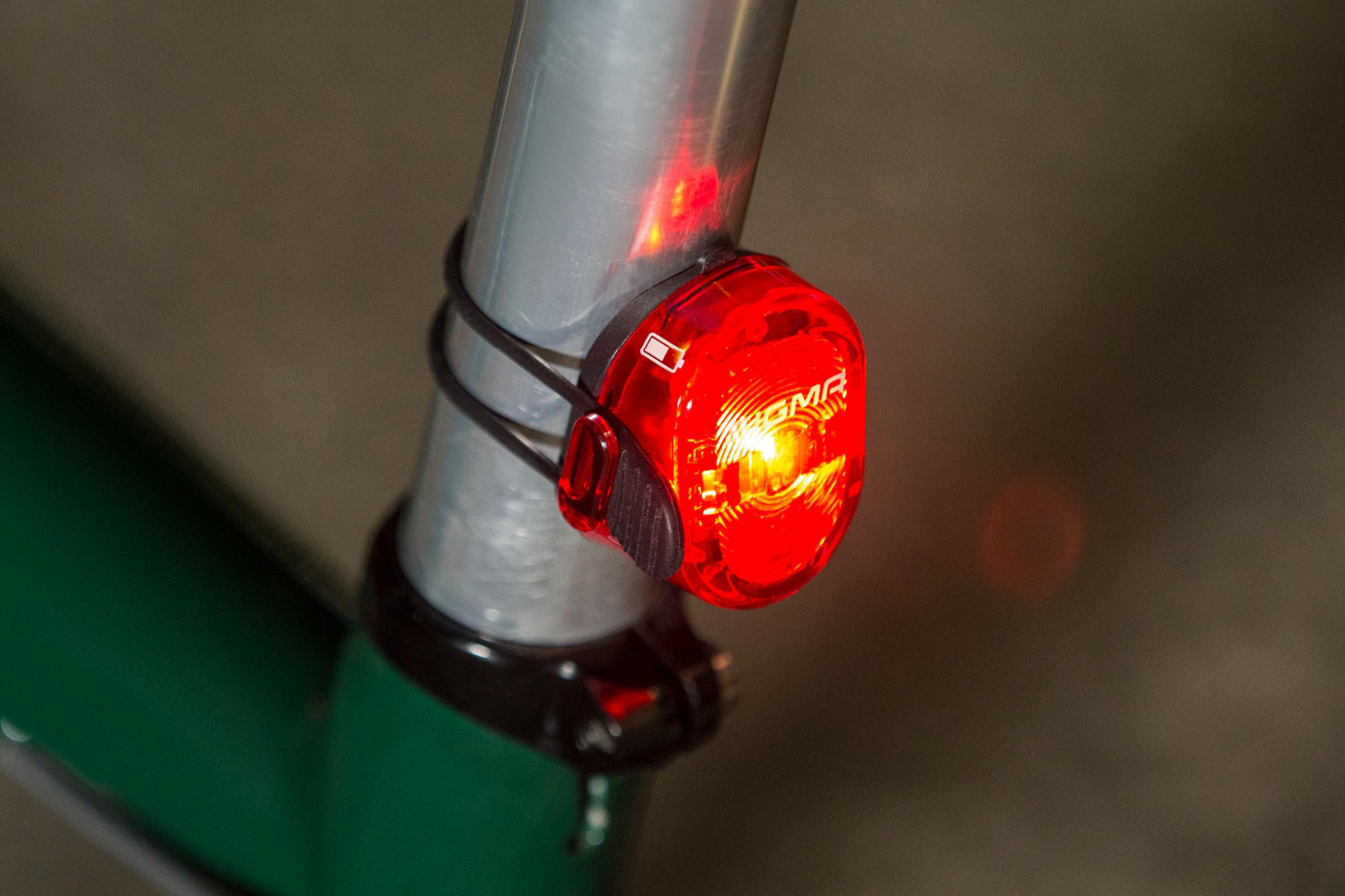 Rotes Fahrradlicht an silberner Fahrradstange befestigt. Schwarzer Riemen hält Licht.