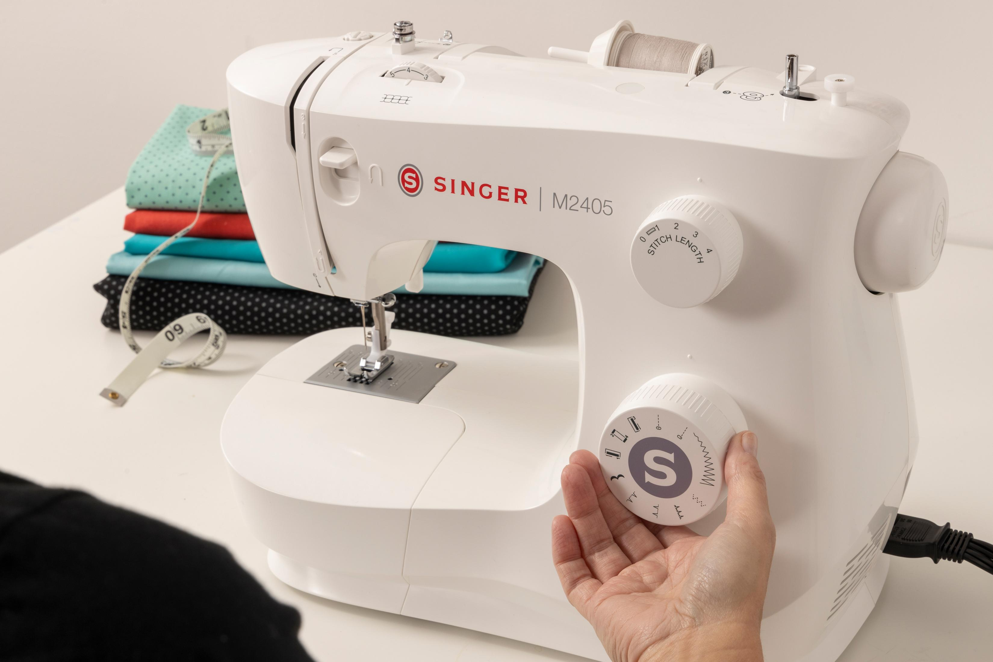 Biała maszyna do szycia, ręka regulująca pokrętło, białe tło.