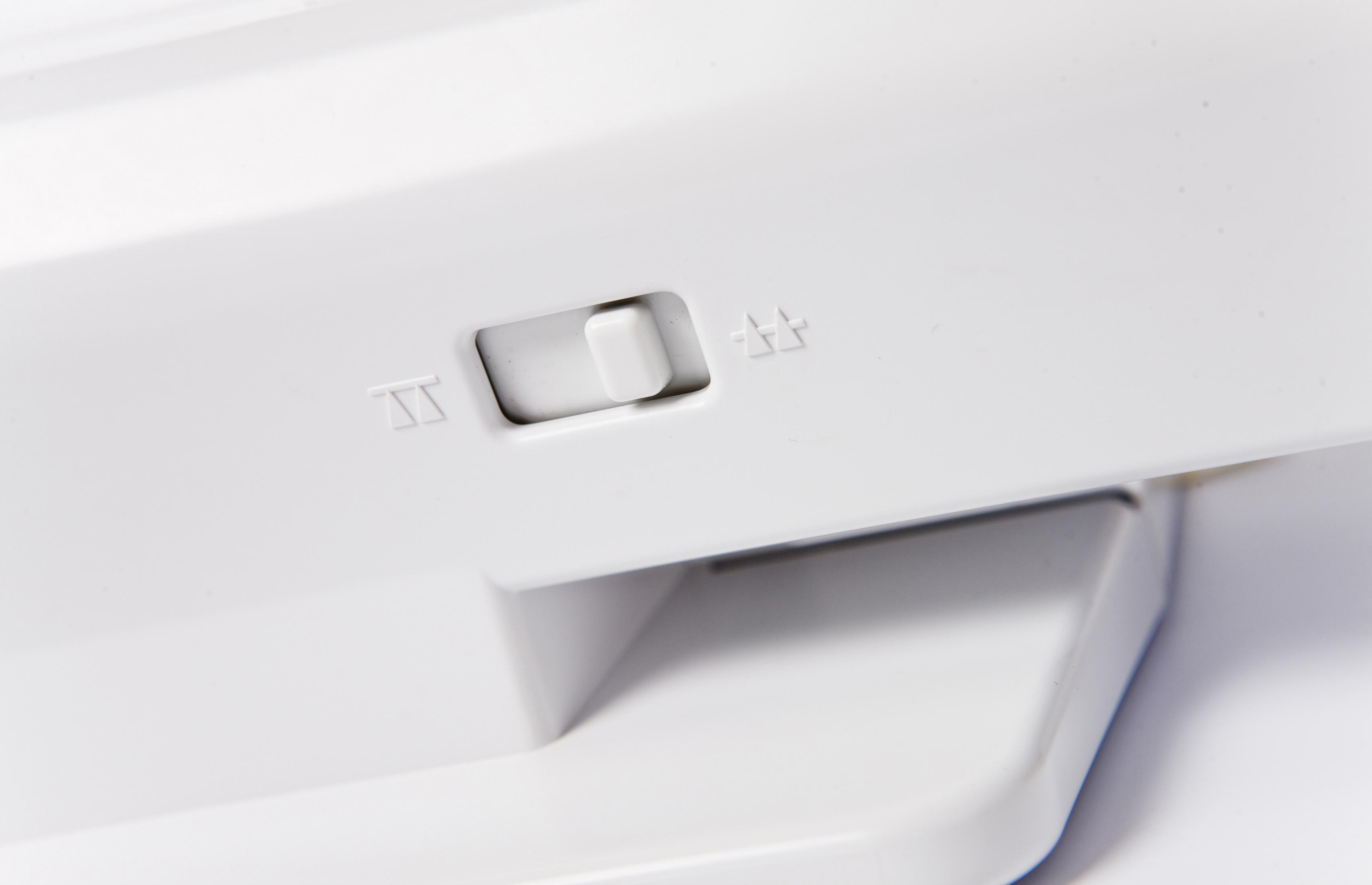 Biały element z tworzywa sztucznego z przełącznikiem i strzałkami, prawdopodobnie część produktu.