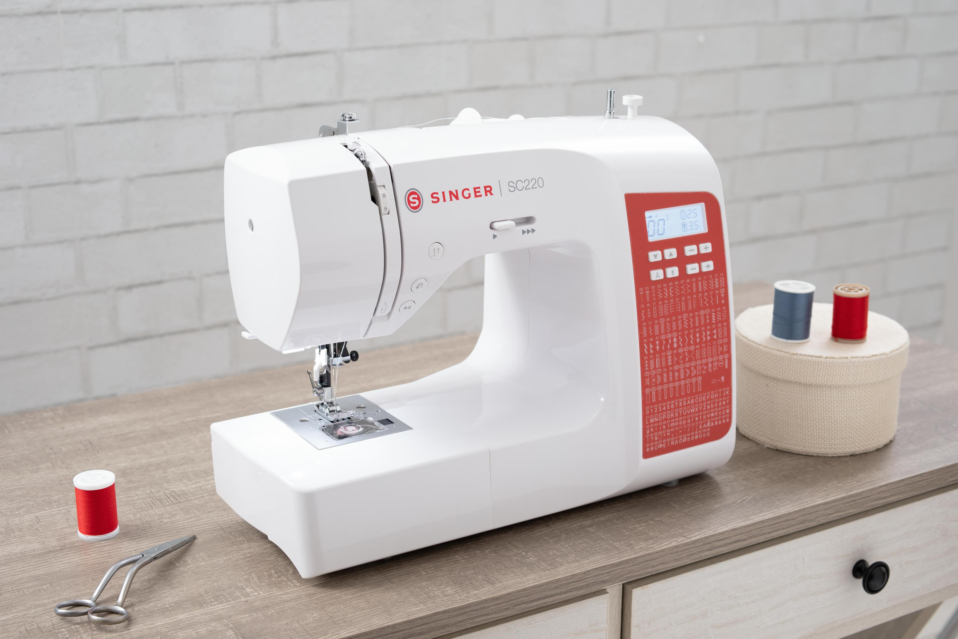 Máquina de coser Singer blanca sobre una mesa de madera con carretes de hilo y tijeras.