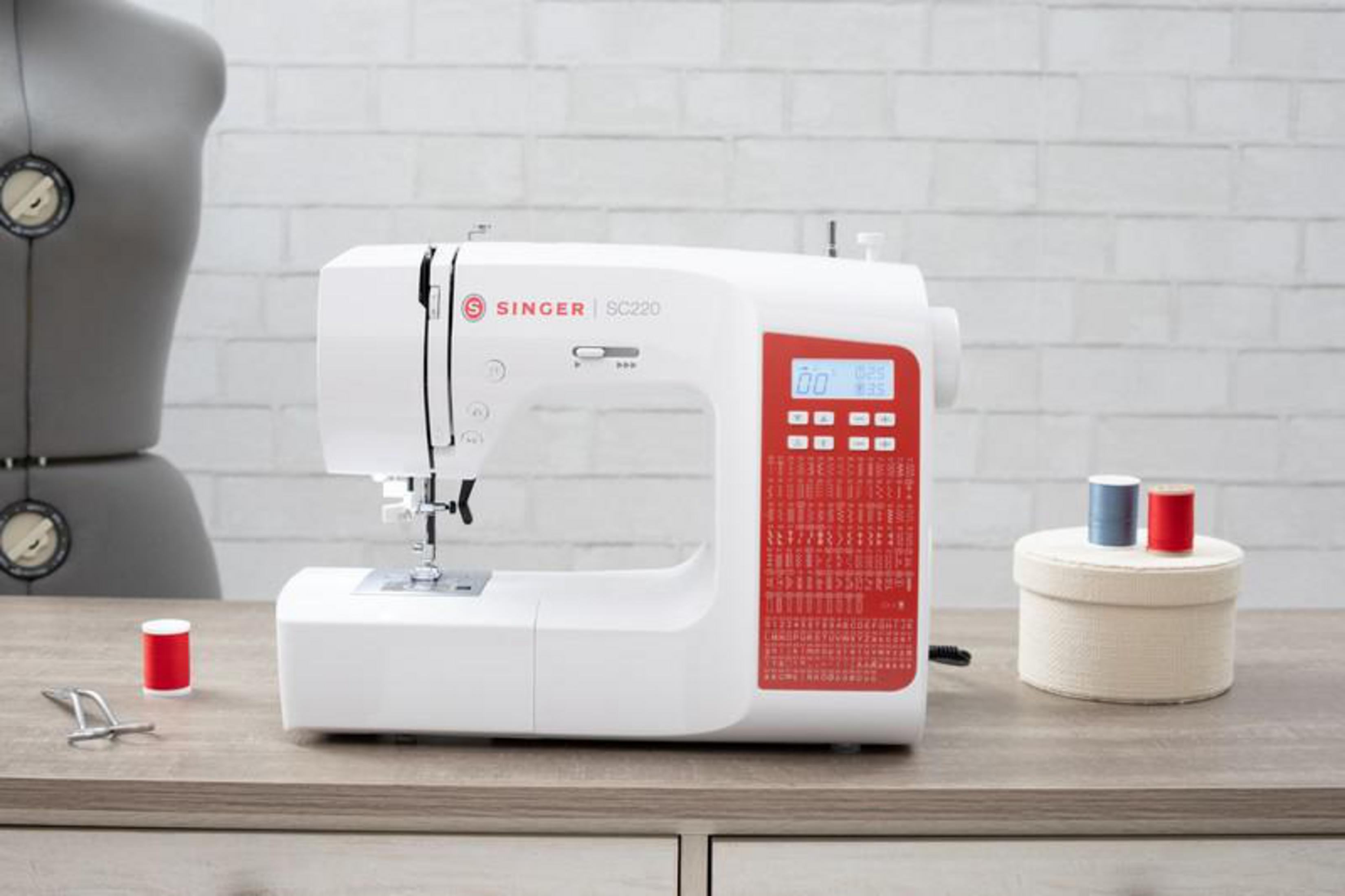 Máquina de coser blanca con detalles rojos sobre mesa de madera.