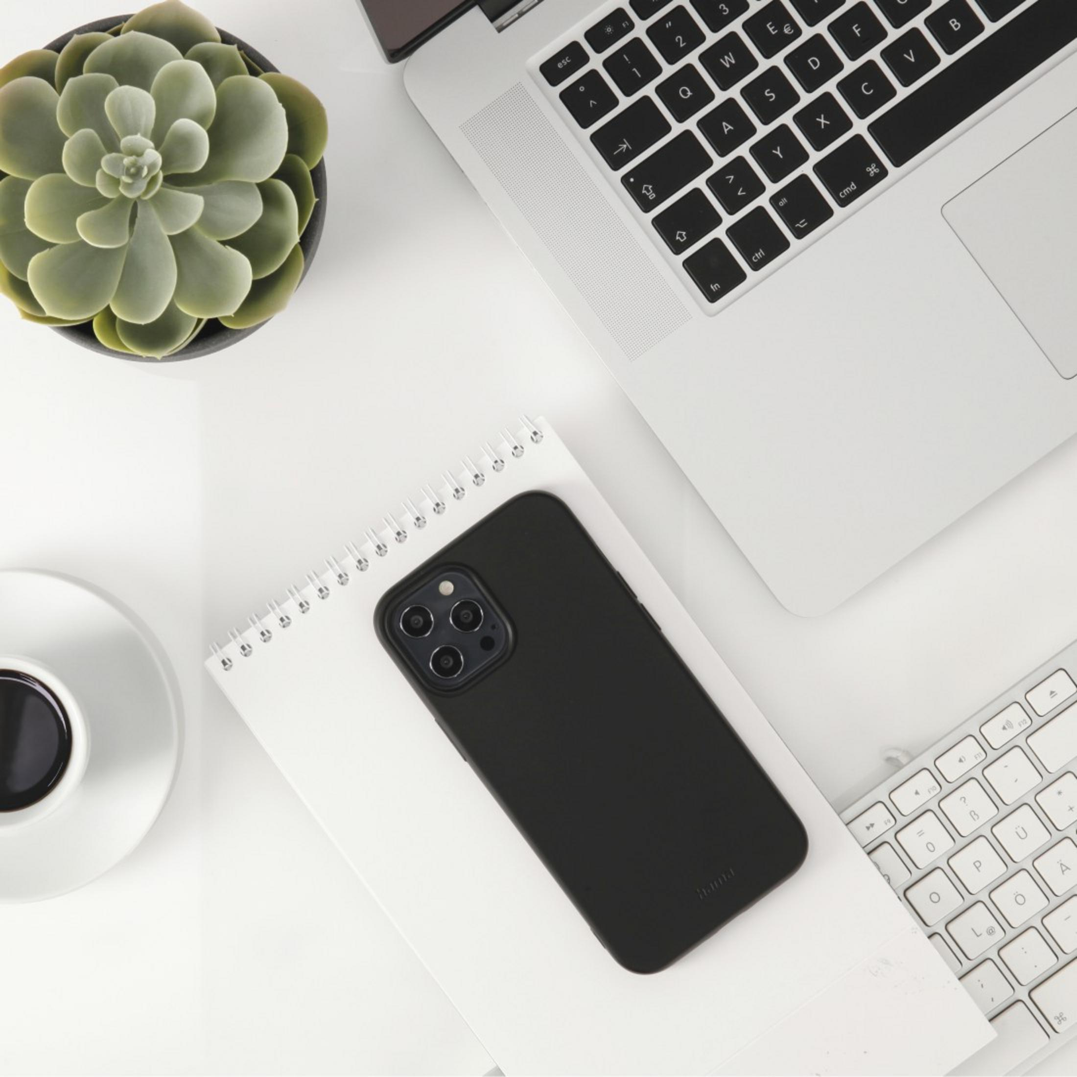 Telefon w czarnym etui leży na notatniku, z laptopem i kawą na białym biurku.