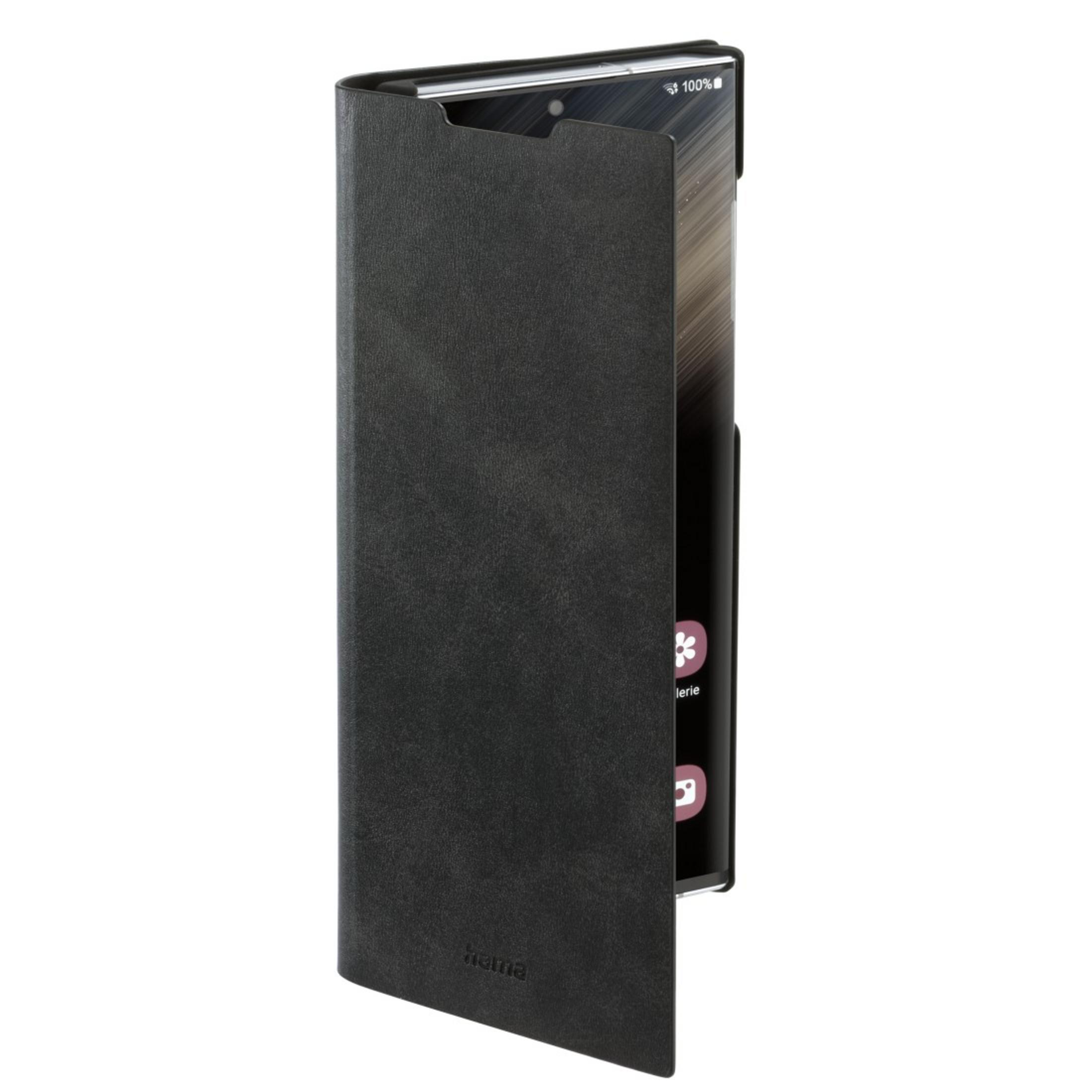 Eine schwarze Handyhülle mit einem Telefon im Inneren wird gezeigt, der Telefonbildschirm ist eingeschaltet, mit einem Hama-Logo auf der Hülle.