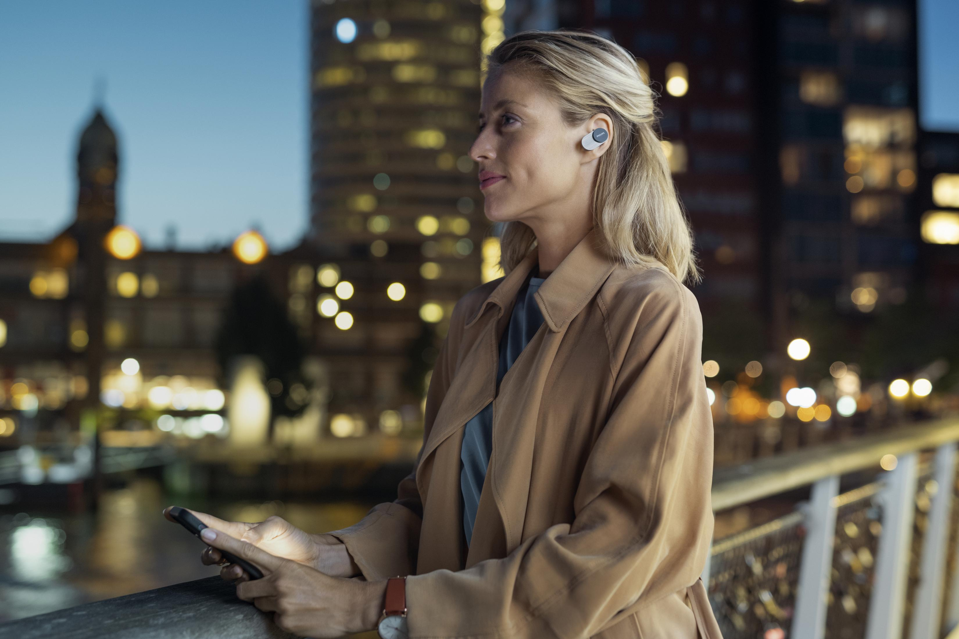 Frau mit Kopfhörern auf einer Brücke bei Nacht. Stadtlichter im Hintergrund.