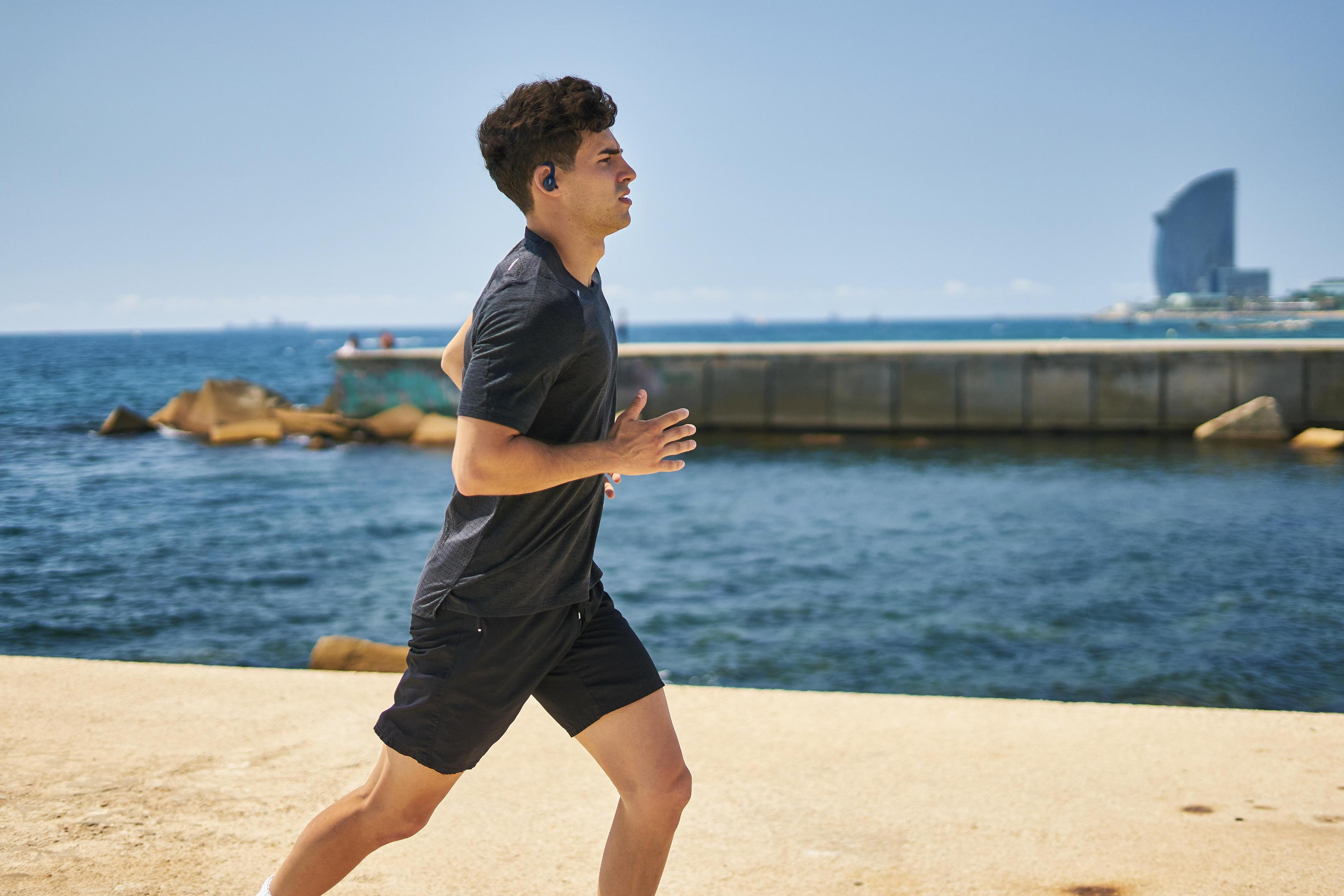 Uomo che corre sulla spiaggia con auricolari, giornata di sole.