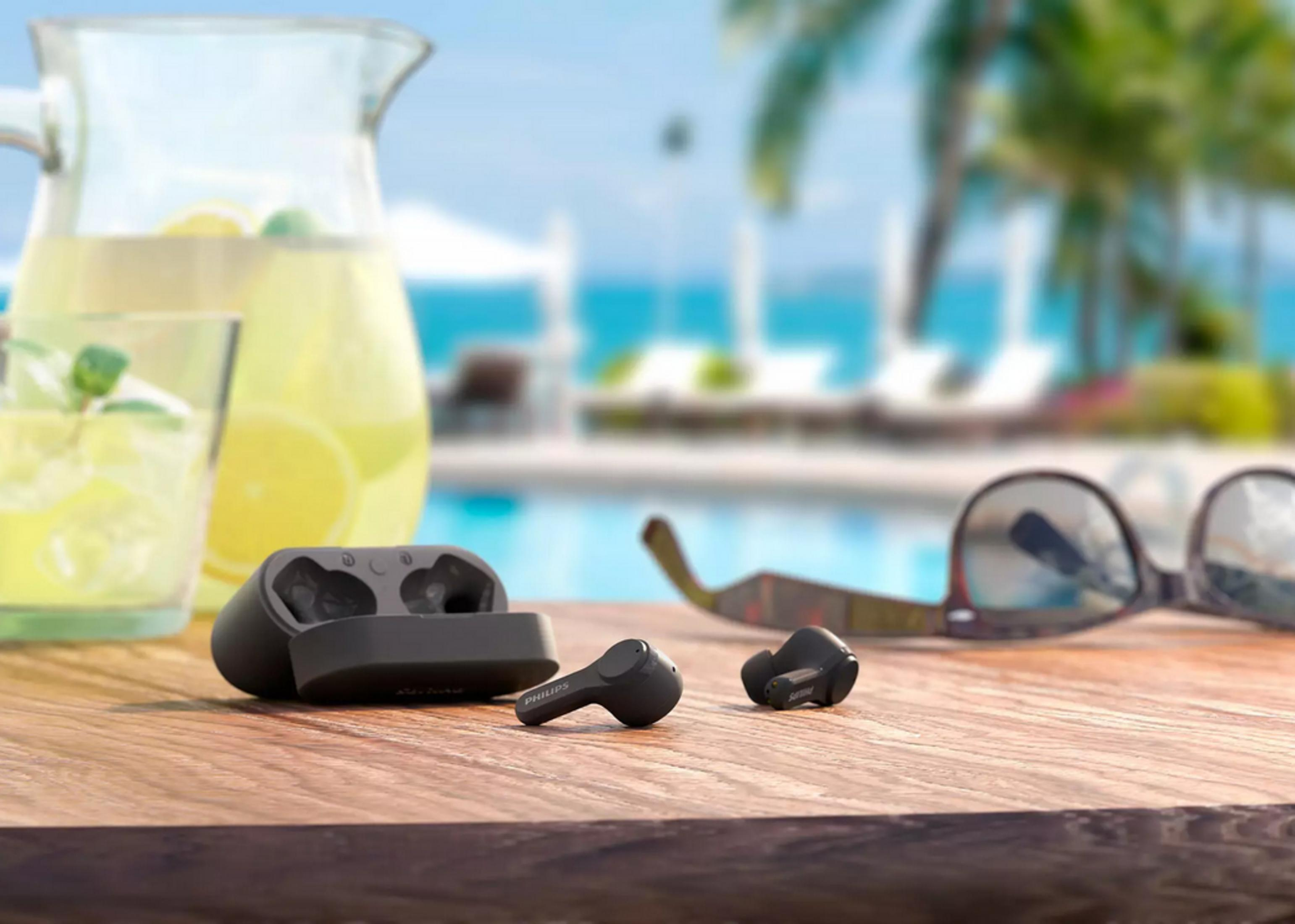 Schwarze Ohrhörer auf Holztisch, neben Limonade und Sonnenbrille. Verschwommener Hintergrund.