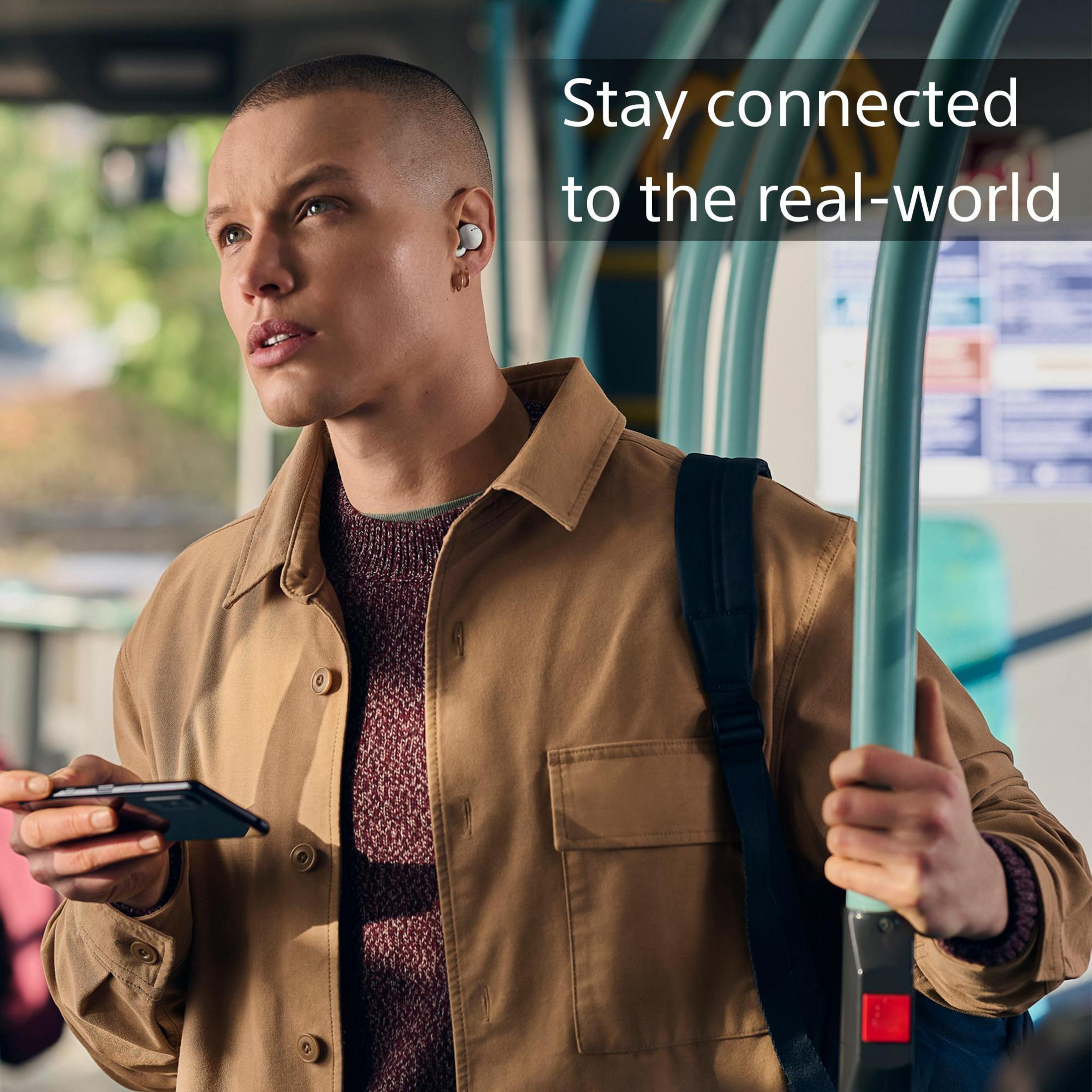 Hombre usando auriculares, sosteniendo un teléfono en un autobús. Texto: Mantente conectado al mundo real.