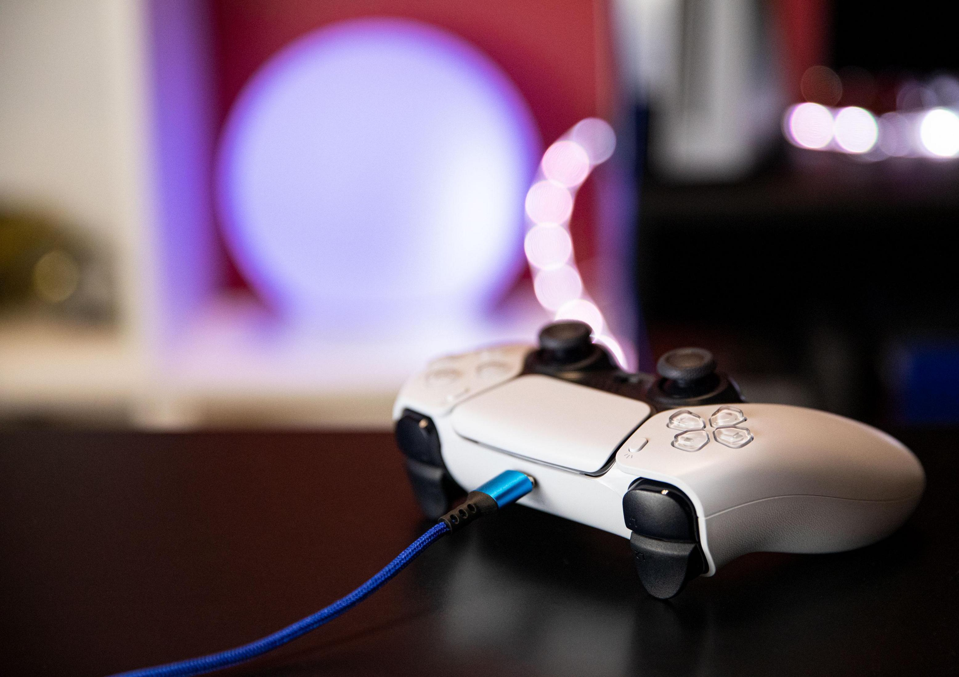 Weißer Gamecontroller mit blauem Kabel. Dunkle Oberfläche mit verschwommenem Licht.