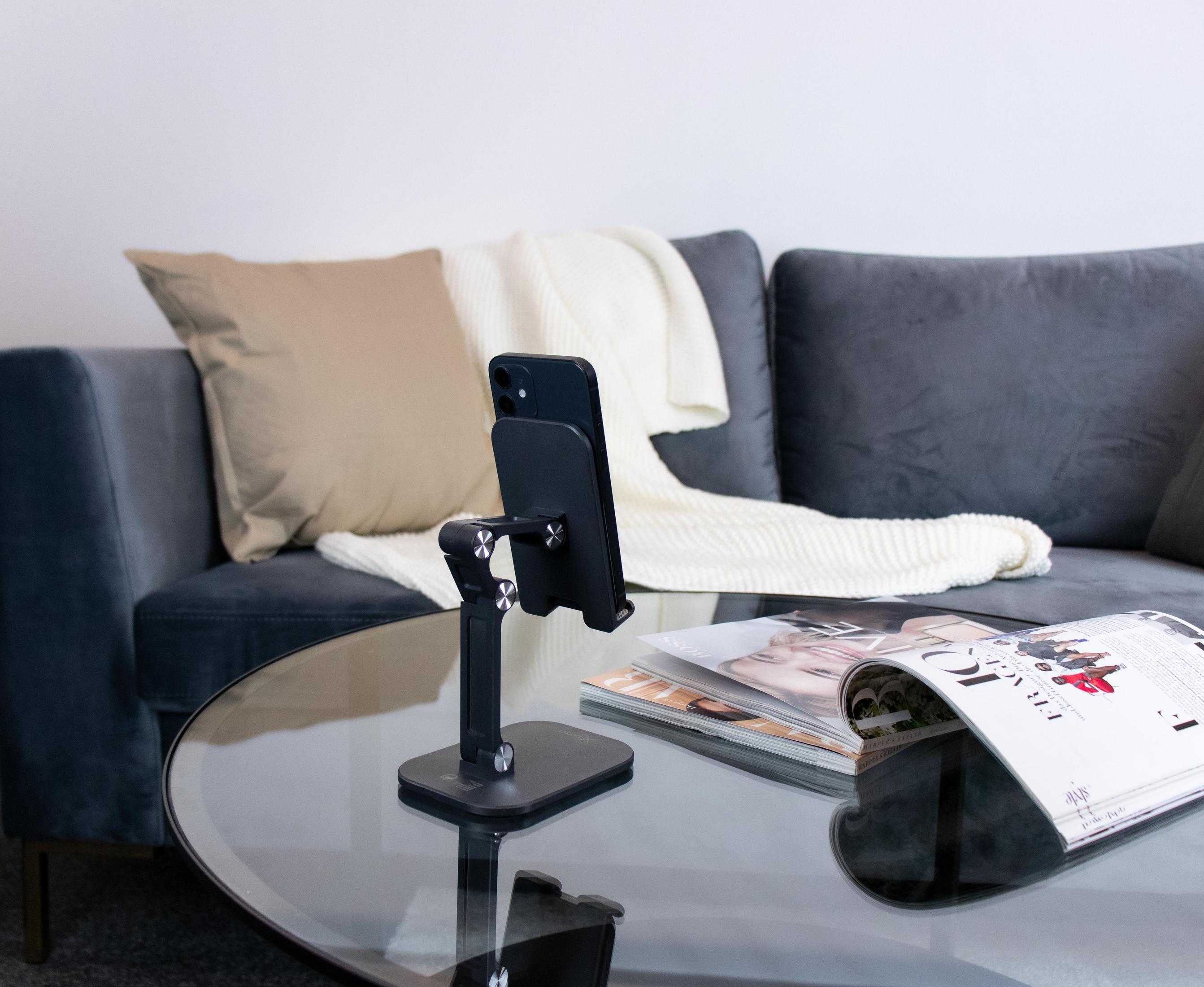 Schwarzes Telefon auf einem Ständer, Zeitschriften und Sofa im Hintergrund.