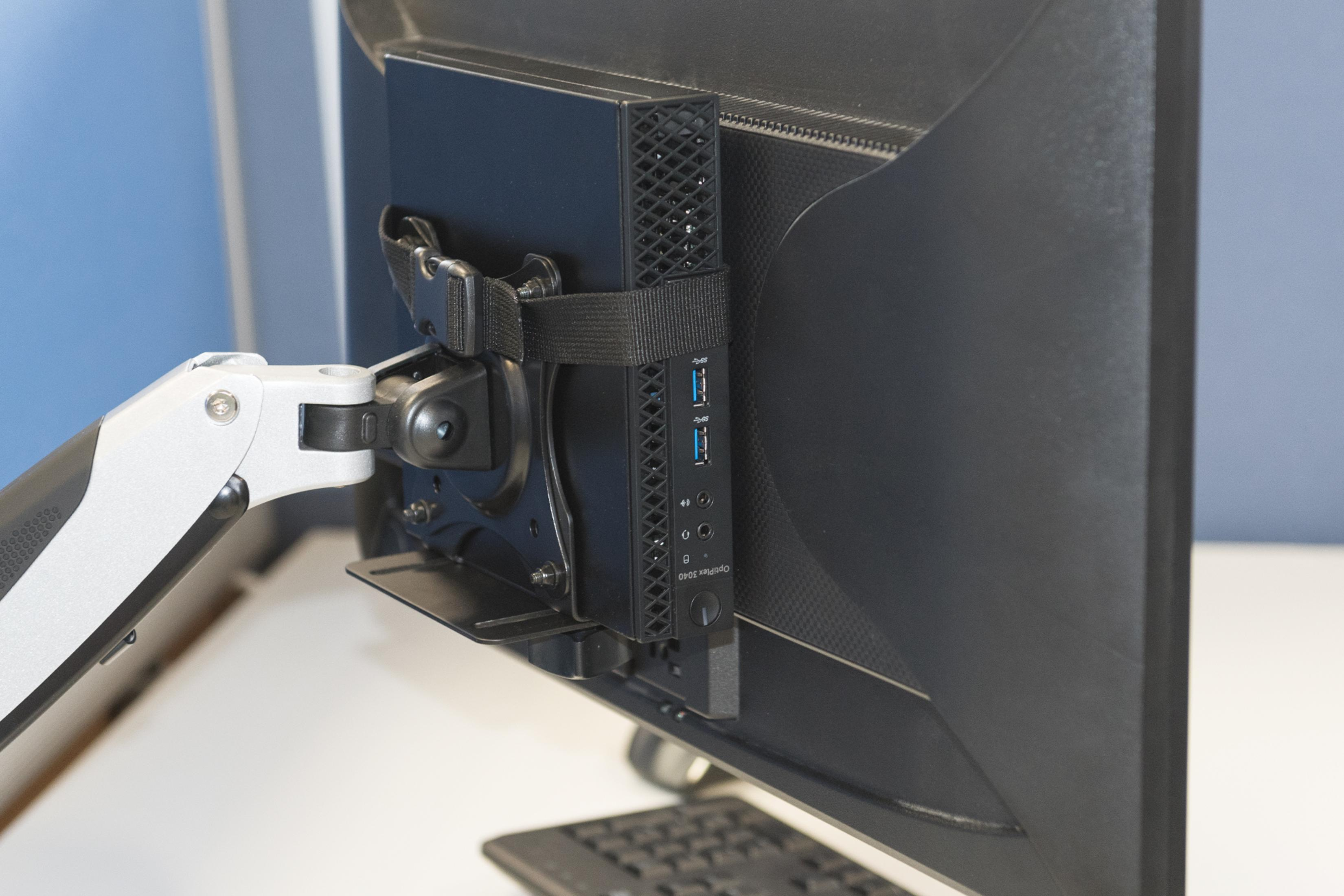 Mały czarny komputer jest zamontowany z tyłu monitora, z podłączonymi przewodami.