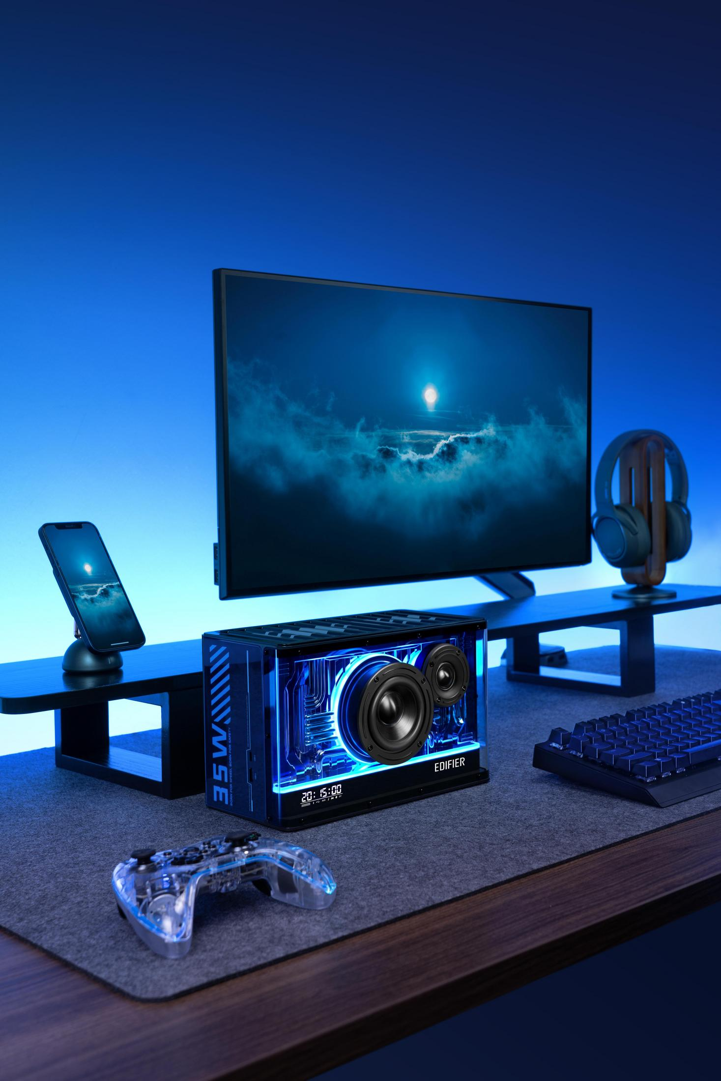 Gaming-Setup mit Lautsprecher, Monitor, Telefon, Controller und Kopfhörern auf einem Schreibtisch.