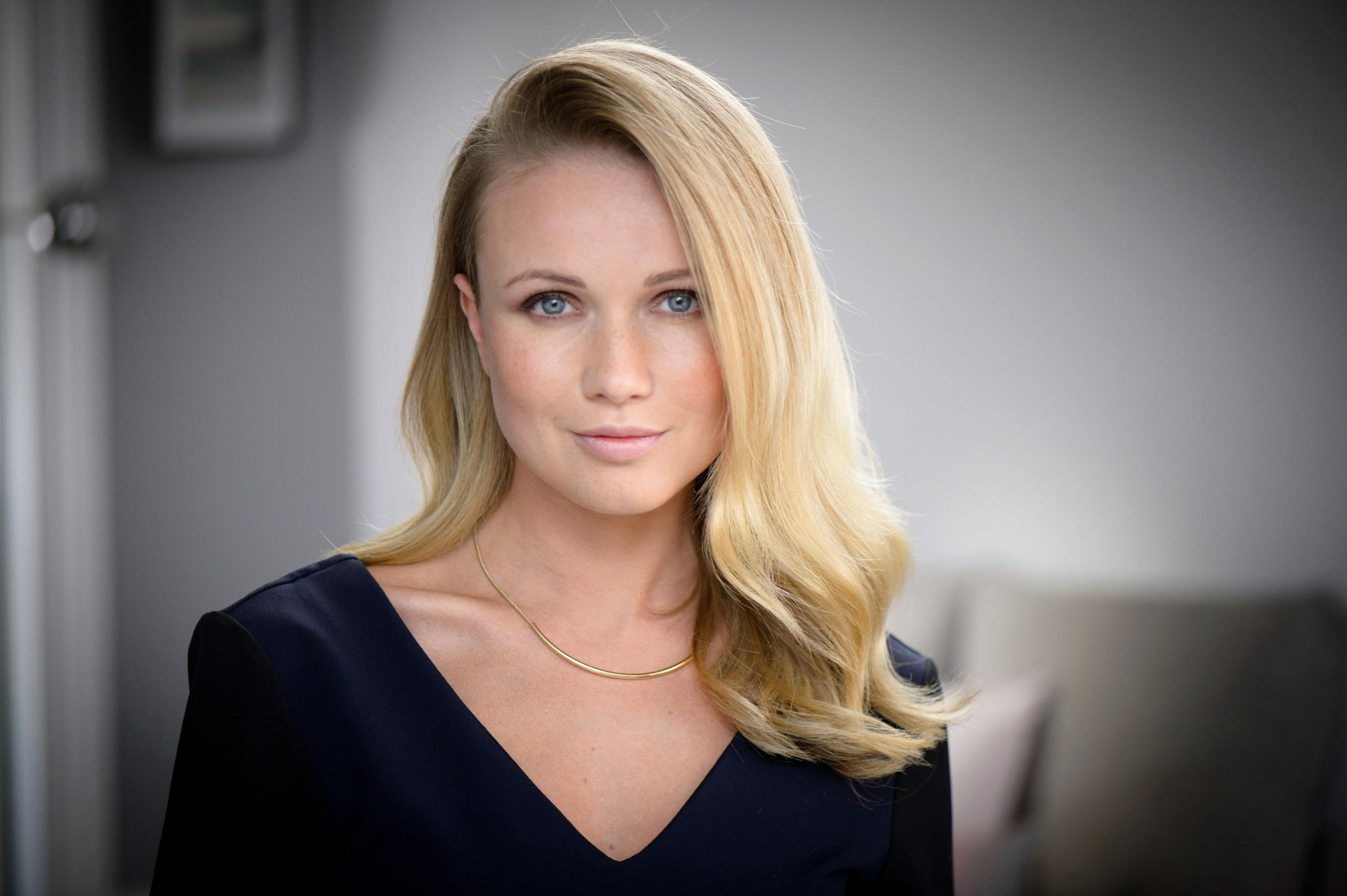 Portret blondynki z niebieskimi oczami. Ma na sobie granatowy top i złoty naszyjnik.